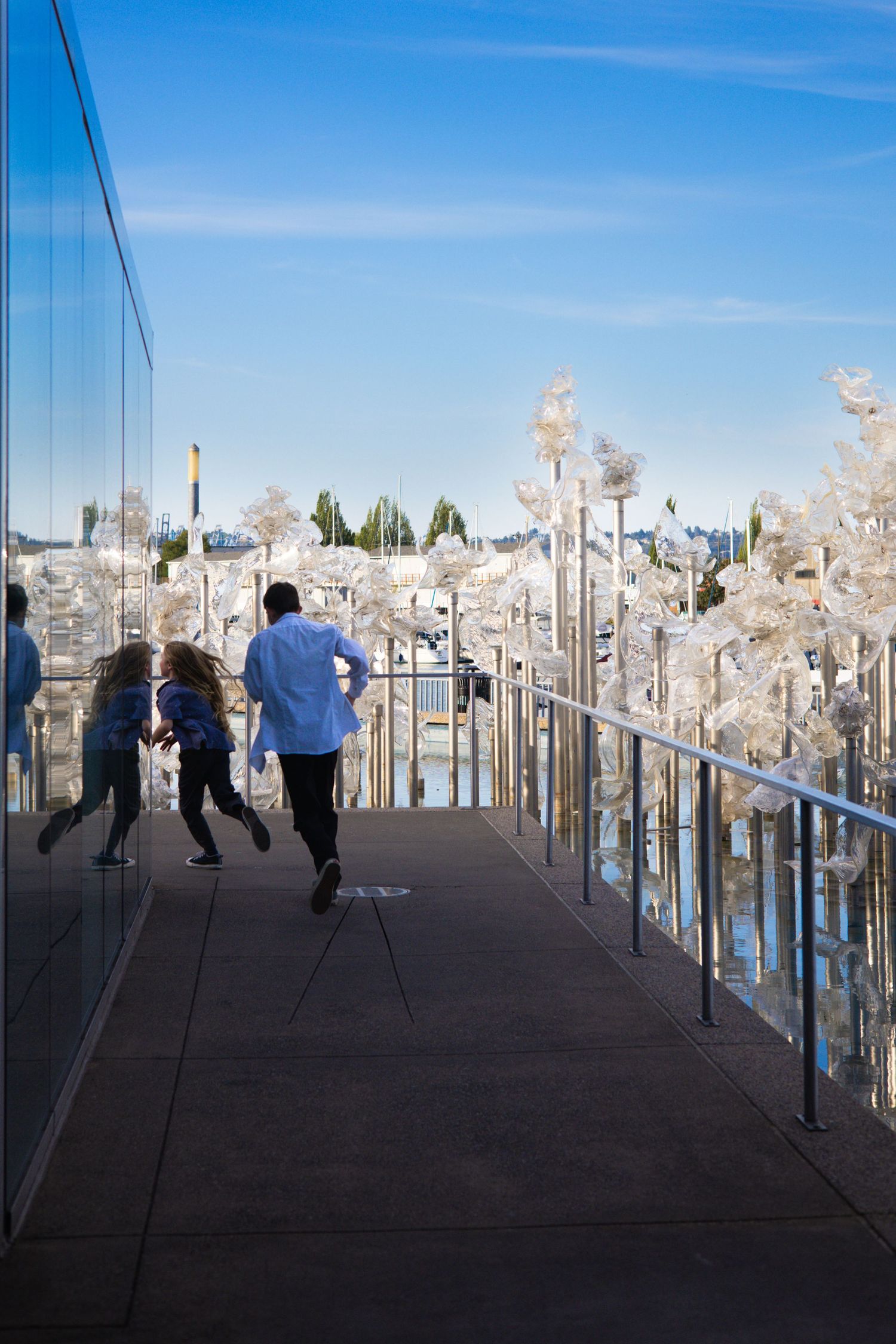 People walking along a modern glass-walled walkway under bright blue skies.