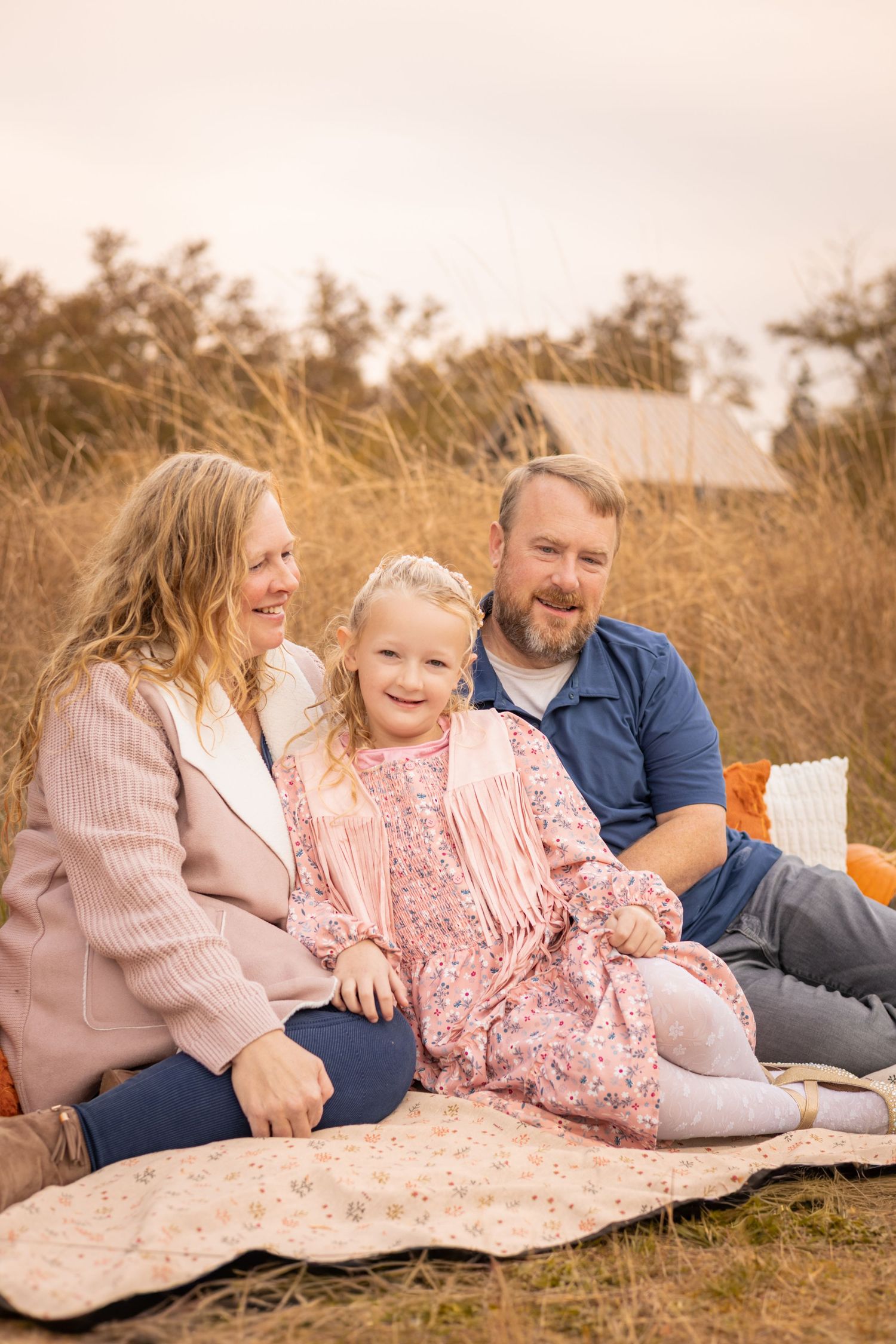A family relaxes together on a blanket in a golden field during sunset.