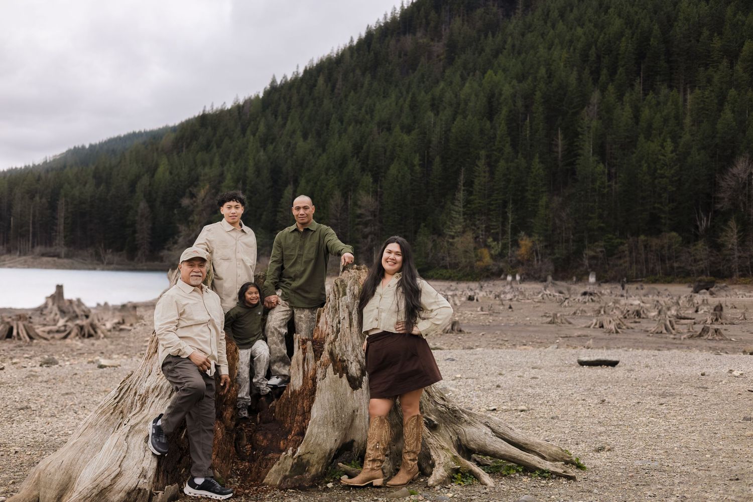 Family of four posing on a large driftwood stump by a lake surrounded by evergreen forest.