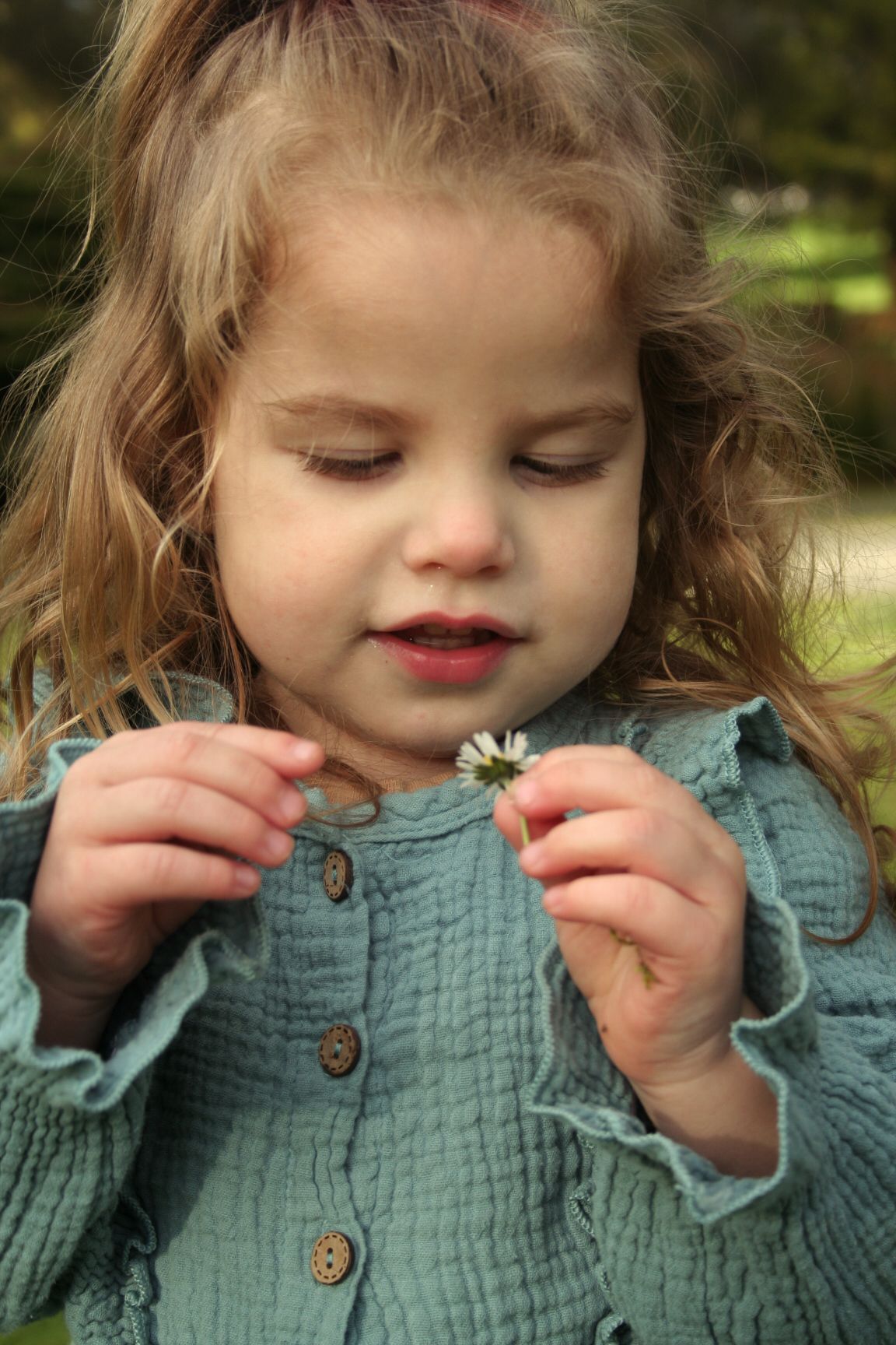 Gentle moment examining a small white flower while wearing a mint button-up dress outdoors.