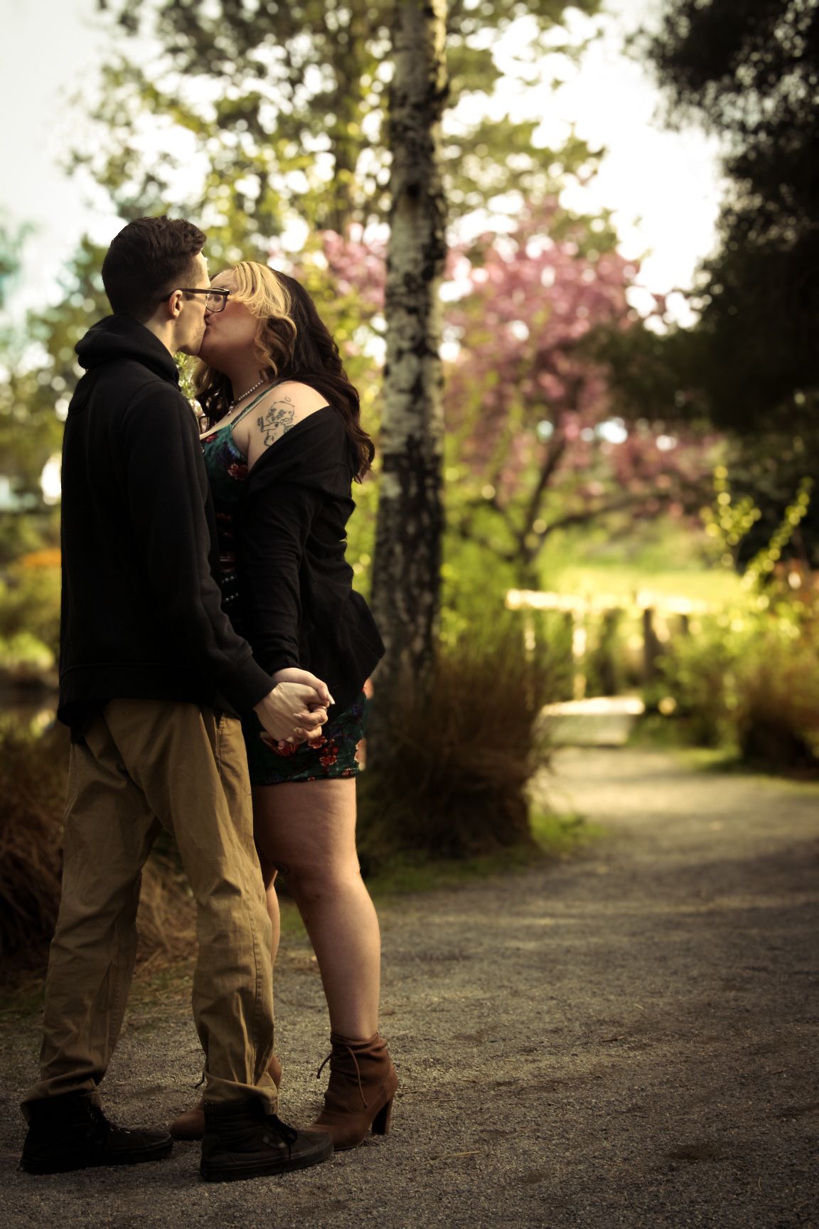 Two people share a tender moment on a sunlit forest path during golden hour.
