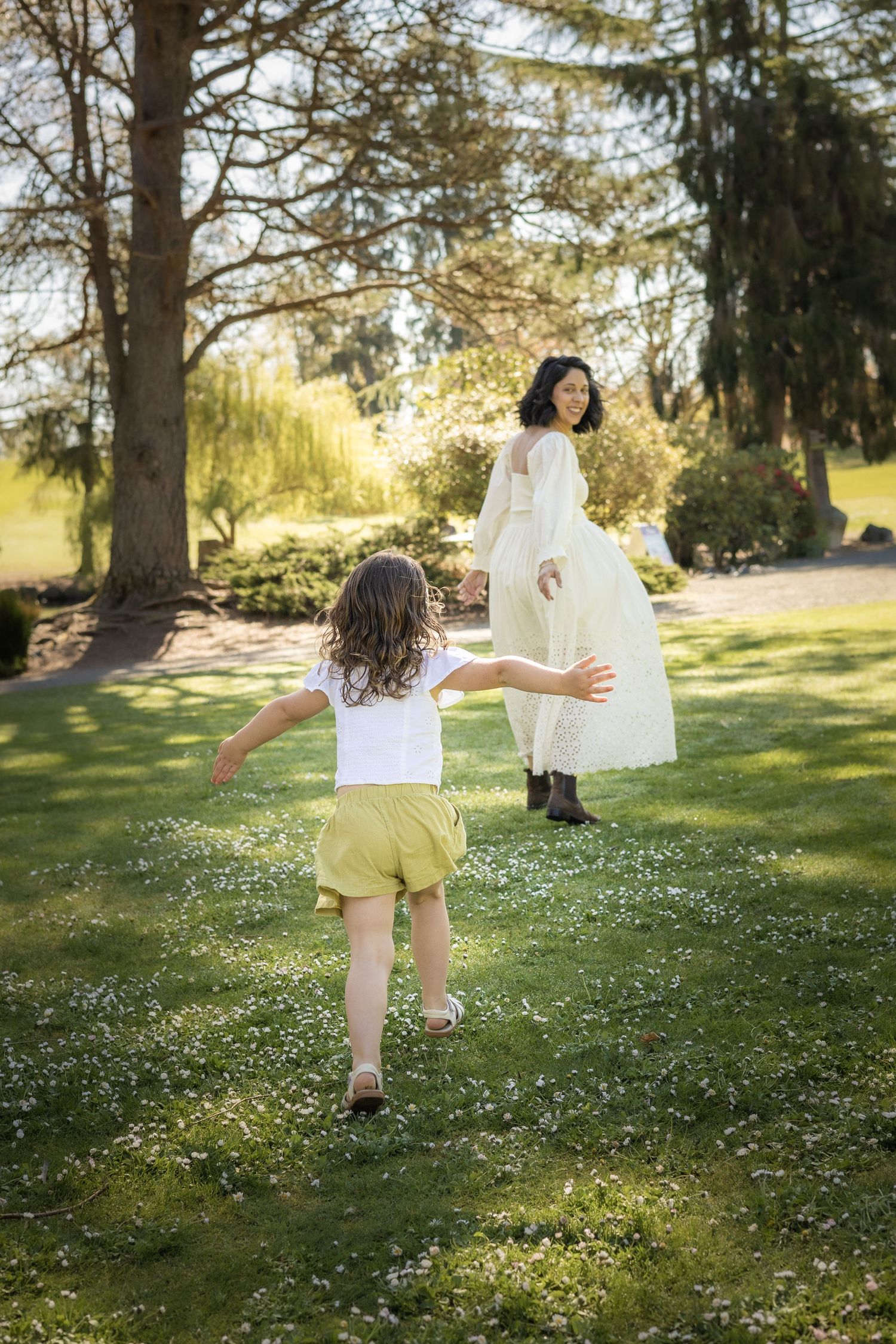 A child runs through a sunny spring meadow dotted with small white flowers while holding a flowing white fabric.