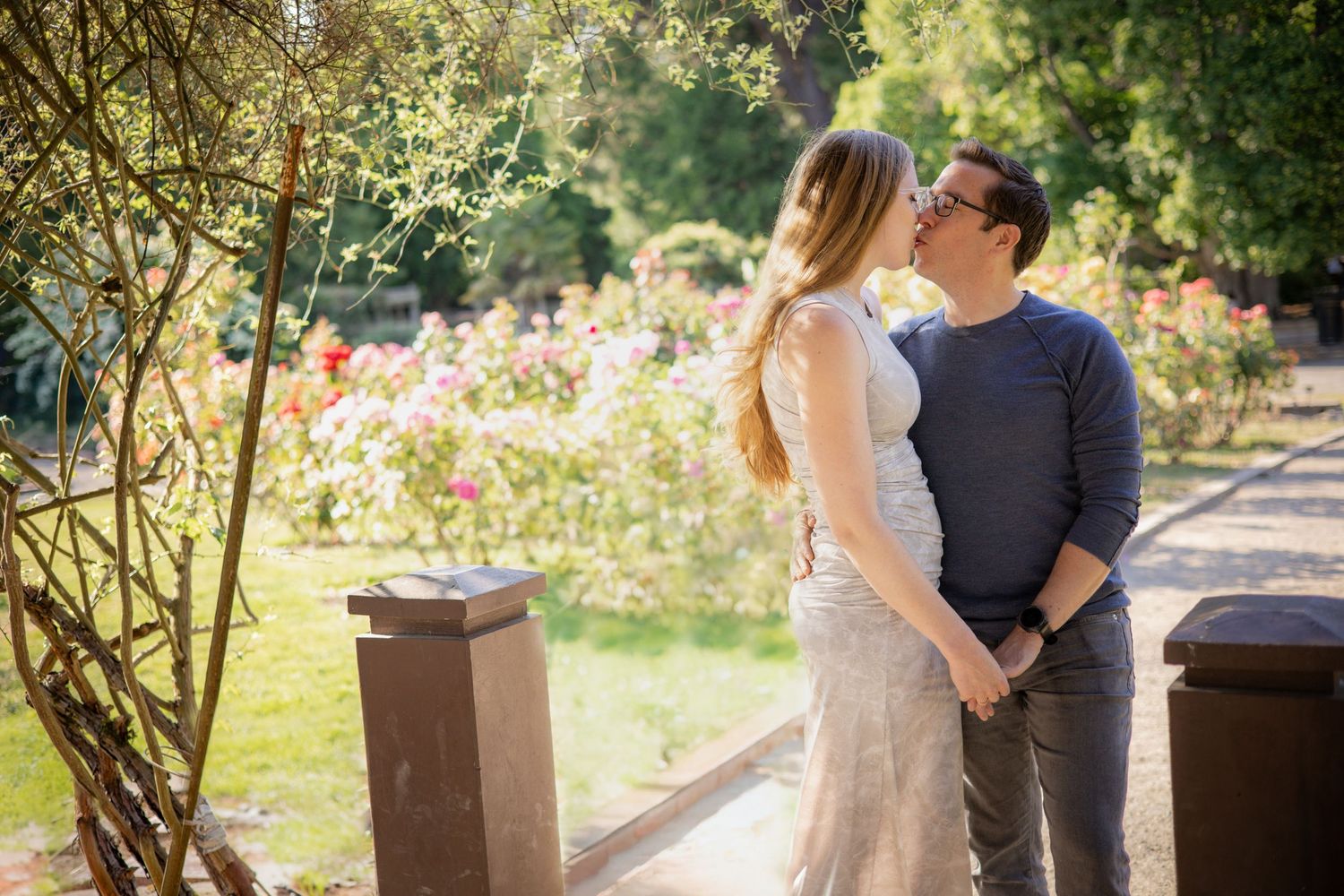 A couple shares a romantic moment in a sunny garden setting with blooming flowers and rustic wooden elements.
