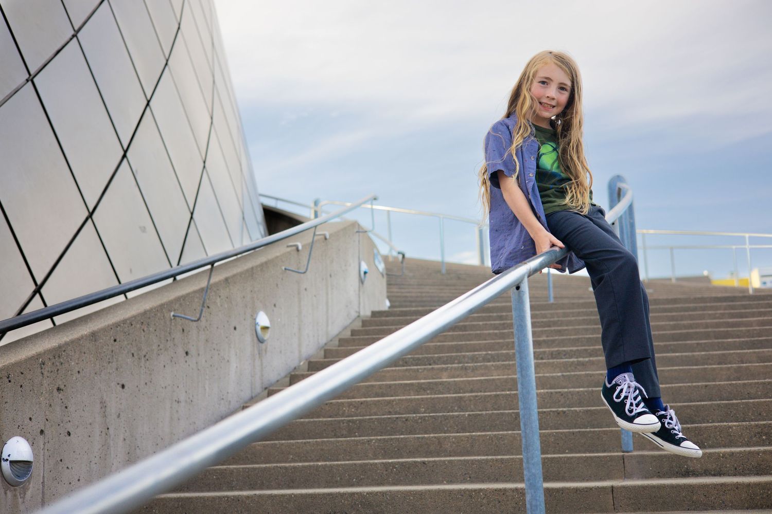 Person sitting on metal railing along concrete steps of modern building.