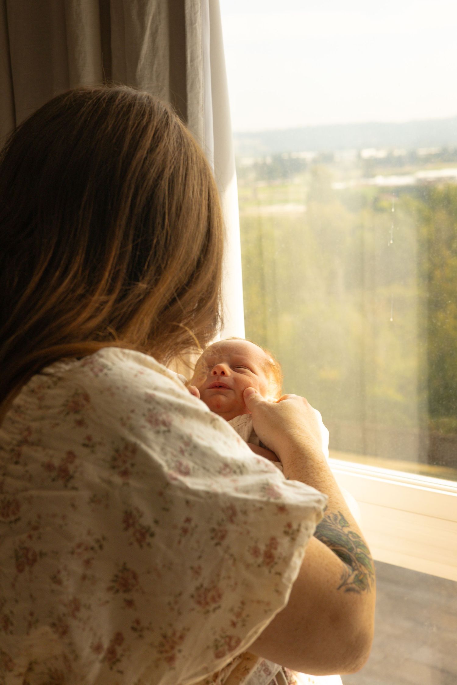 Mom holding newborn by window with valley view — romantic, cinematic lifestyle photography in Tacoma, Puyallup, South Sound WA