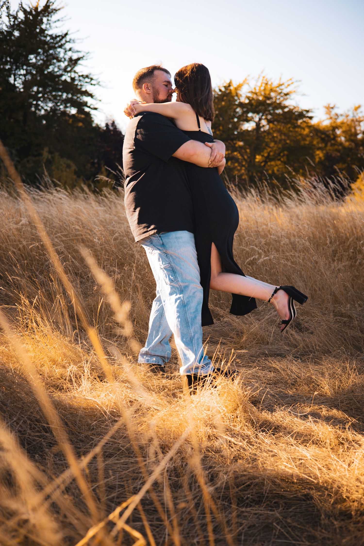 Couple embraces in sunlit field of golden grass during sunset.