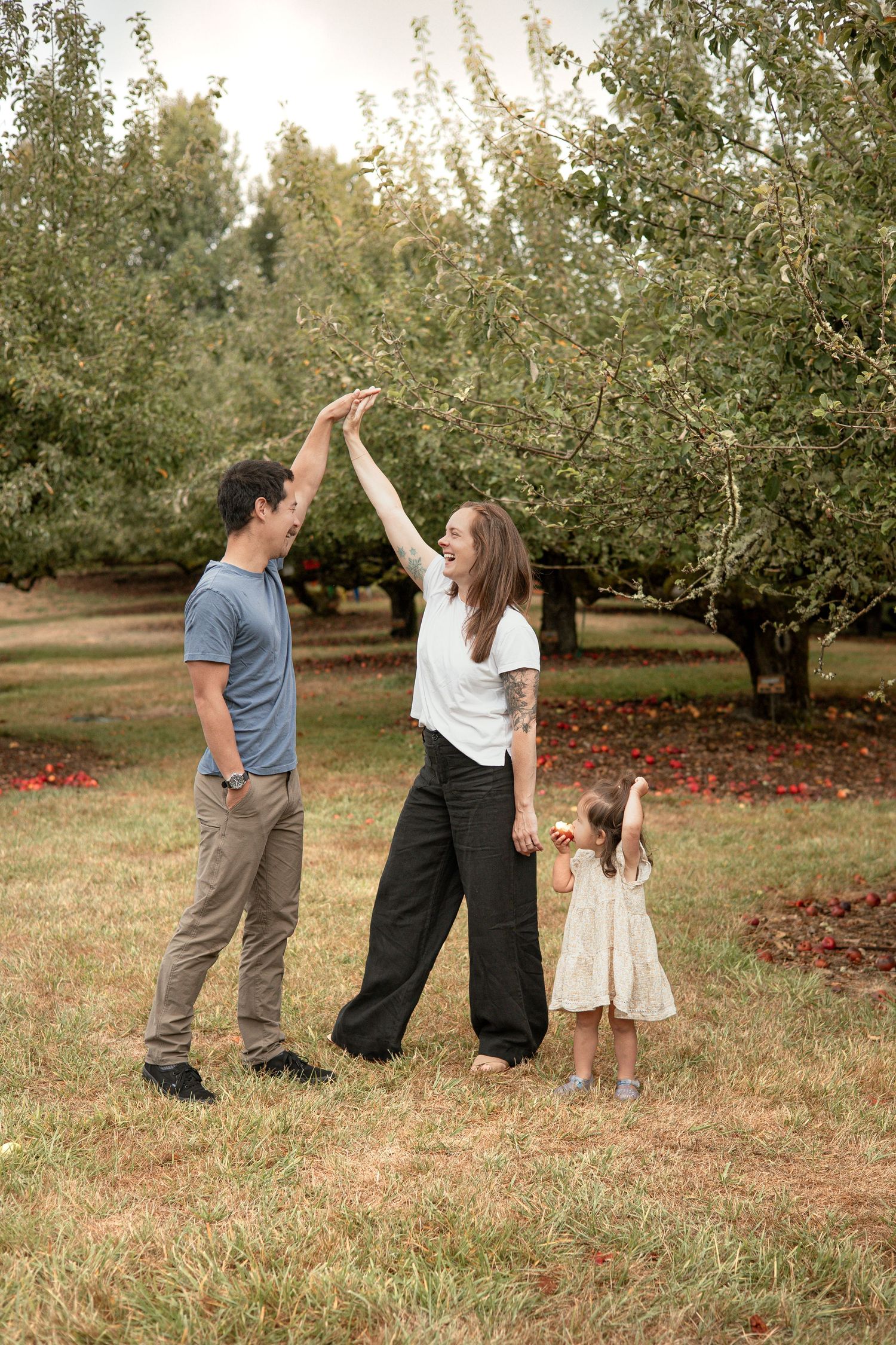 A couple shares a celebratory high five together in an apple orchard during a sunny autumn day.