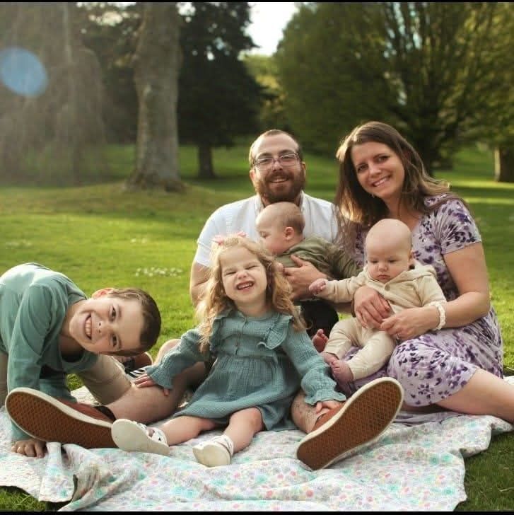 Family relaxing together on a patterned blanket in a sunny park setting.