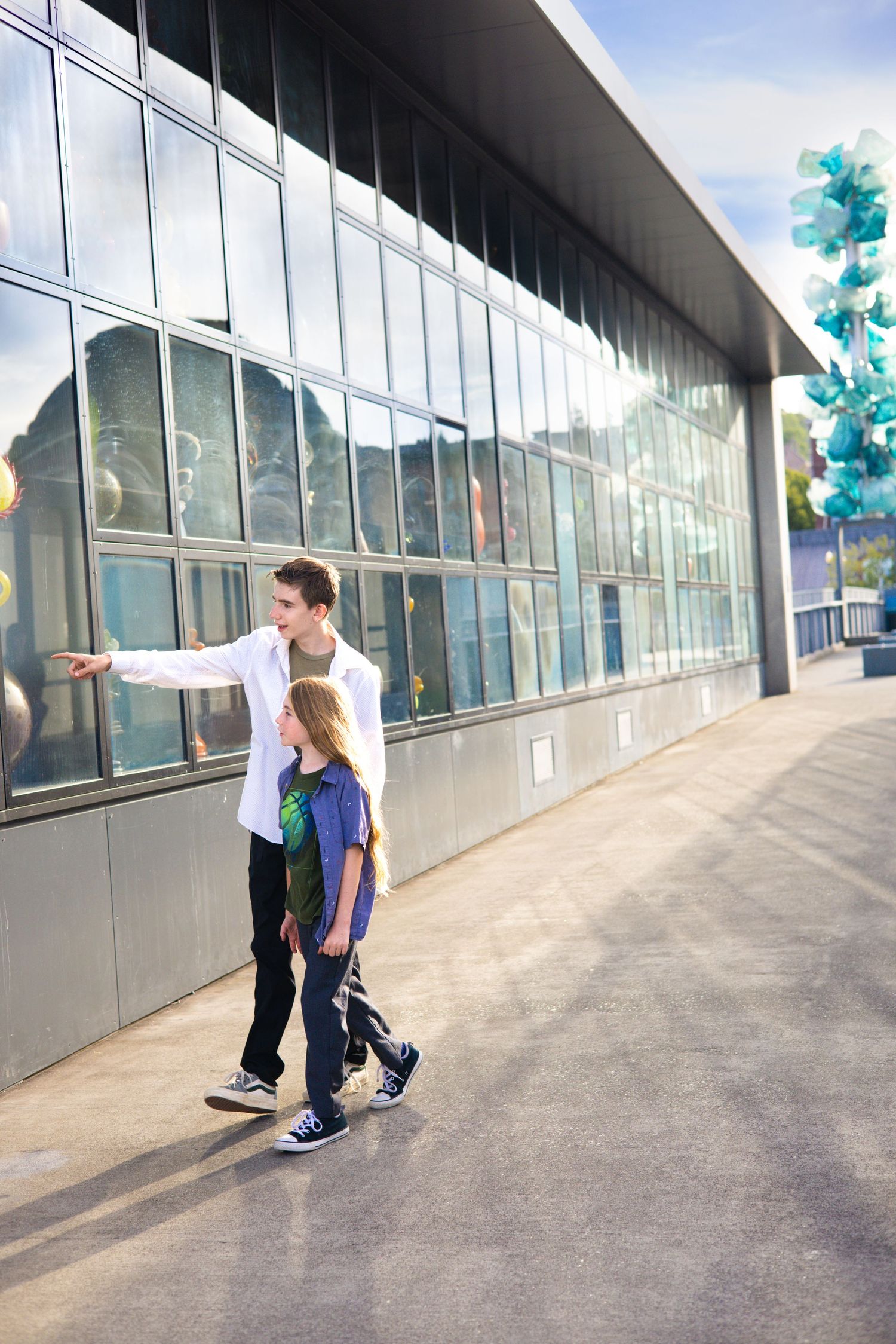 Two people walking along modern glass building exterior on sunny day.