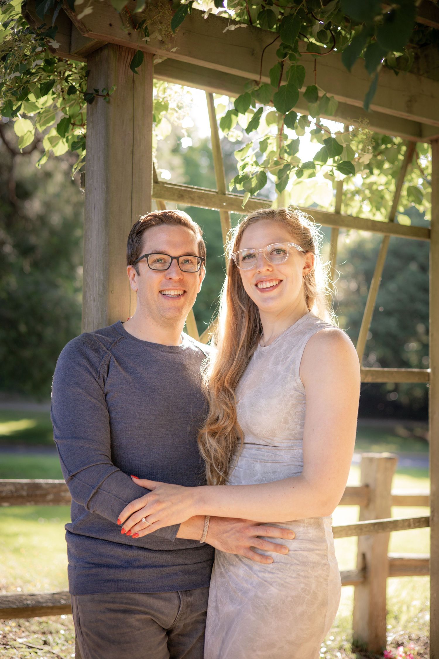 Loving couple poses together under a rustic wooden gazebo in natural sunlight.