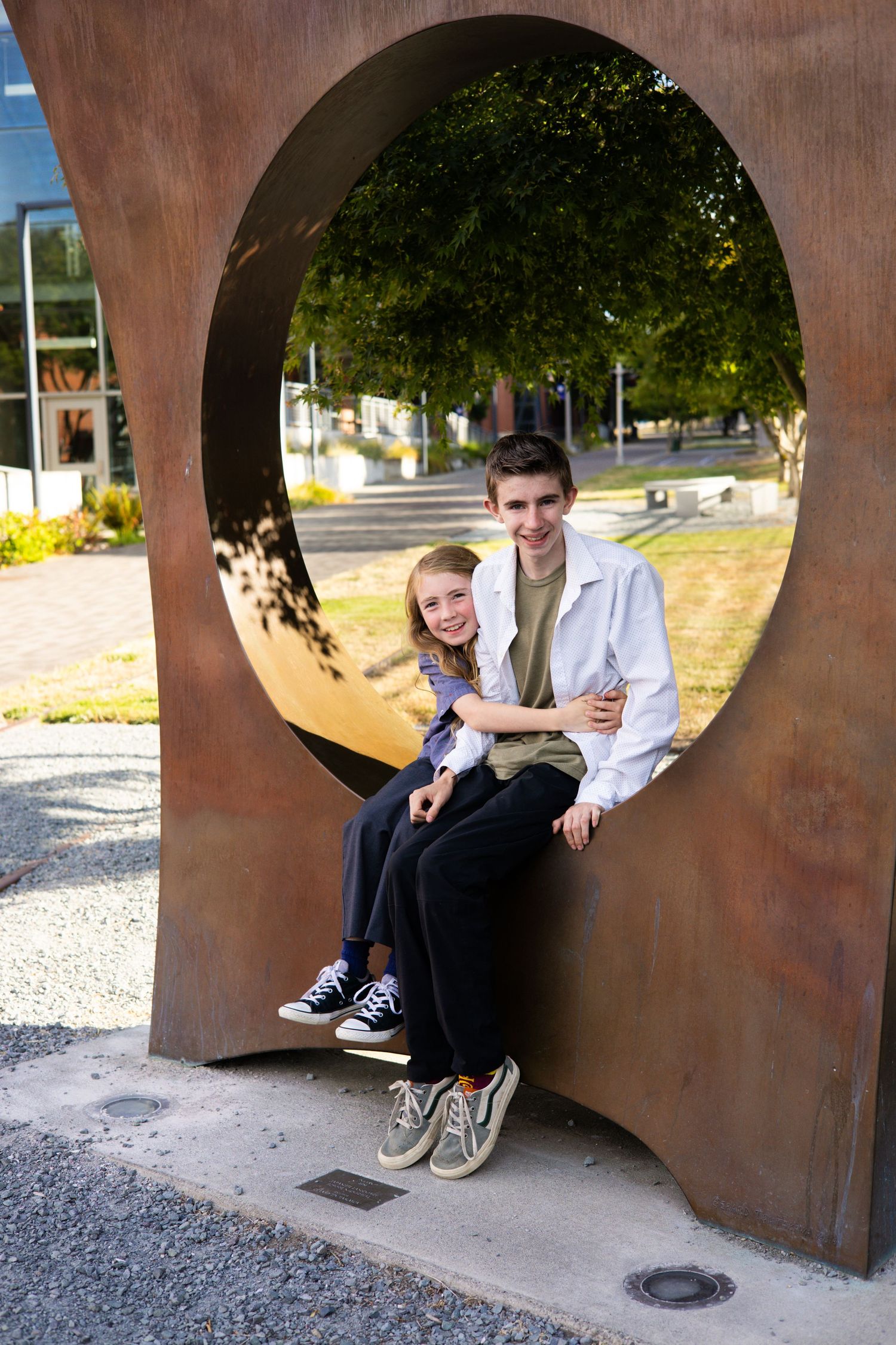Large circular metal sculpture creating a tunnel-like space with gravel ground.