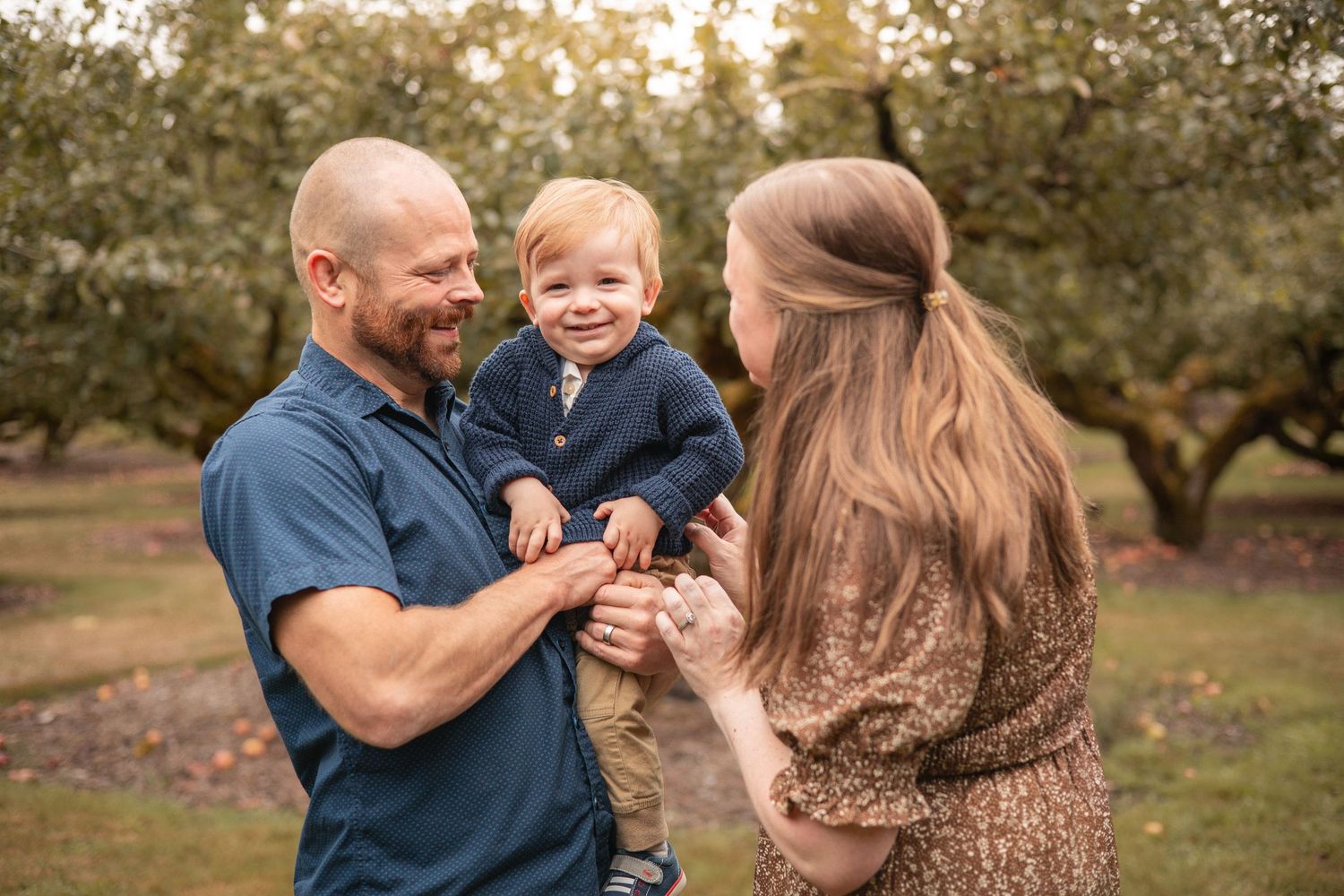 A family enjoys a playful moment together in an autumn orchard setting during a golden hour photoshoot.