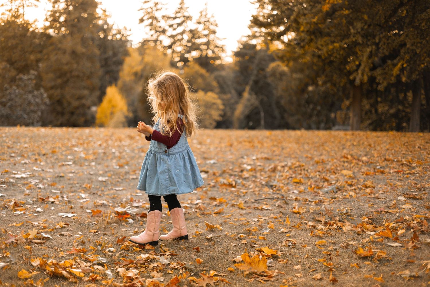 Children play and run through fallen autumn leaves in a park during golden hour sunset.