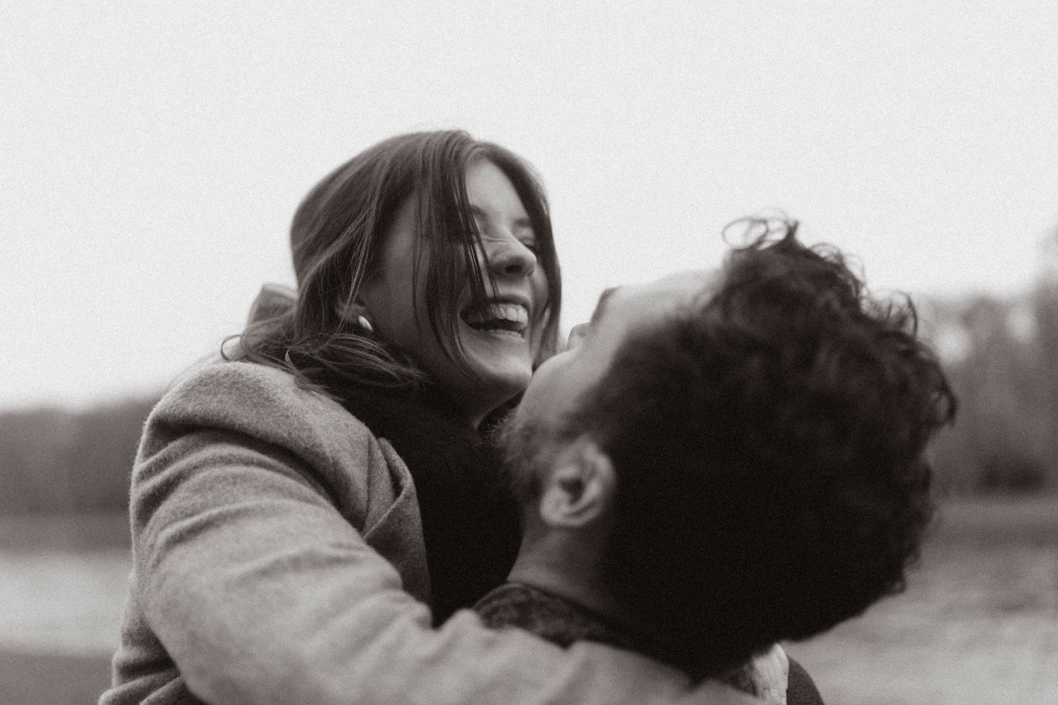 Black and white photo of a joyful couple embracing and laughing together outdoors.