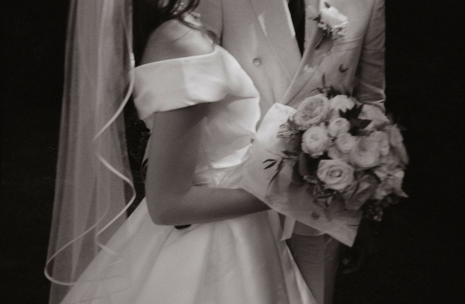 A close-up black and white photo of a couple at their wedding, with the bride holding a round bouquet of roses.