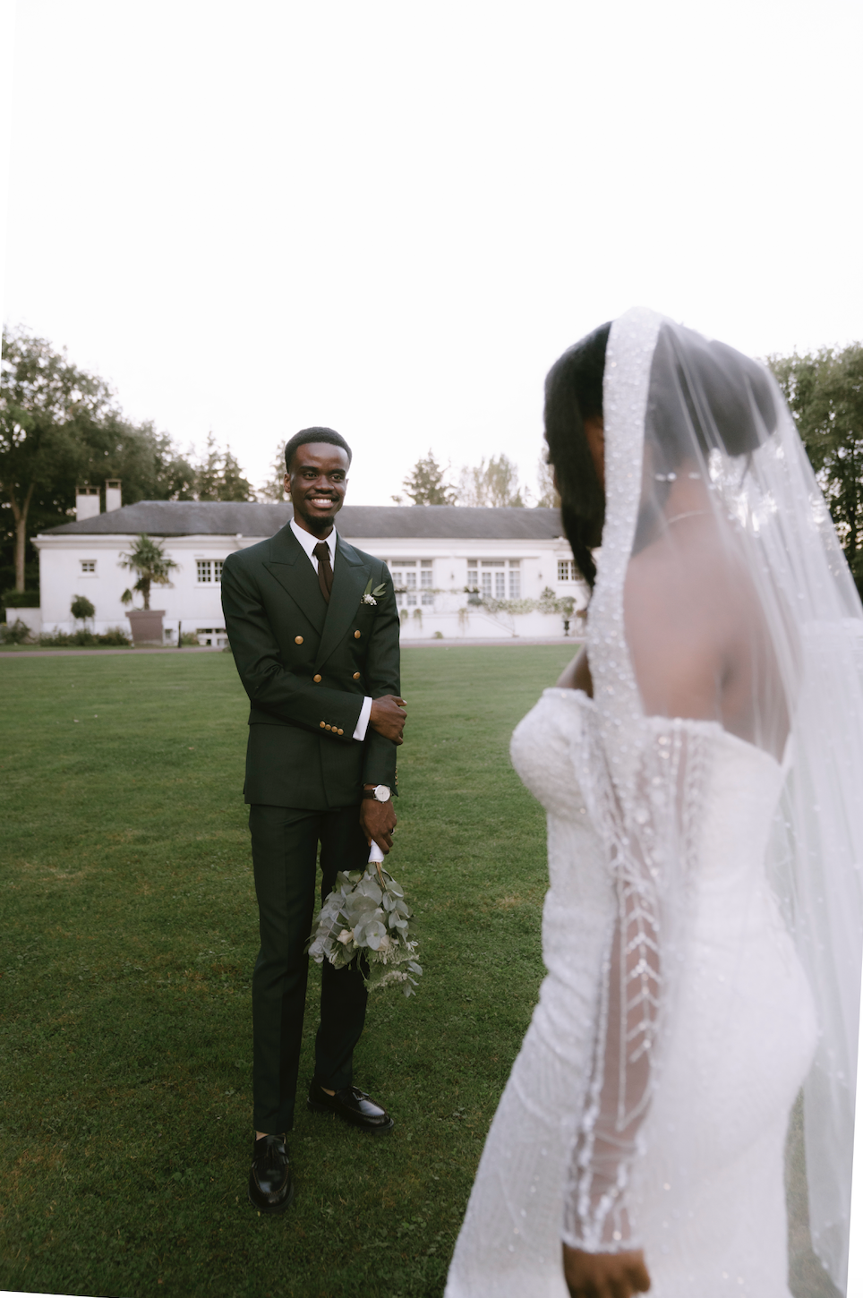 Wedding couple on manicured lawn with bride in lace dress and groom in dark suit.