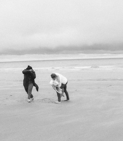 Two people playfully run and laugh on a cloudy beach.