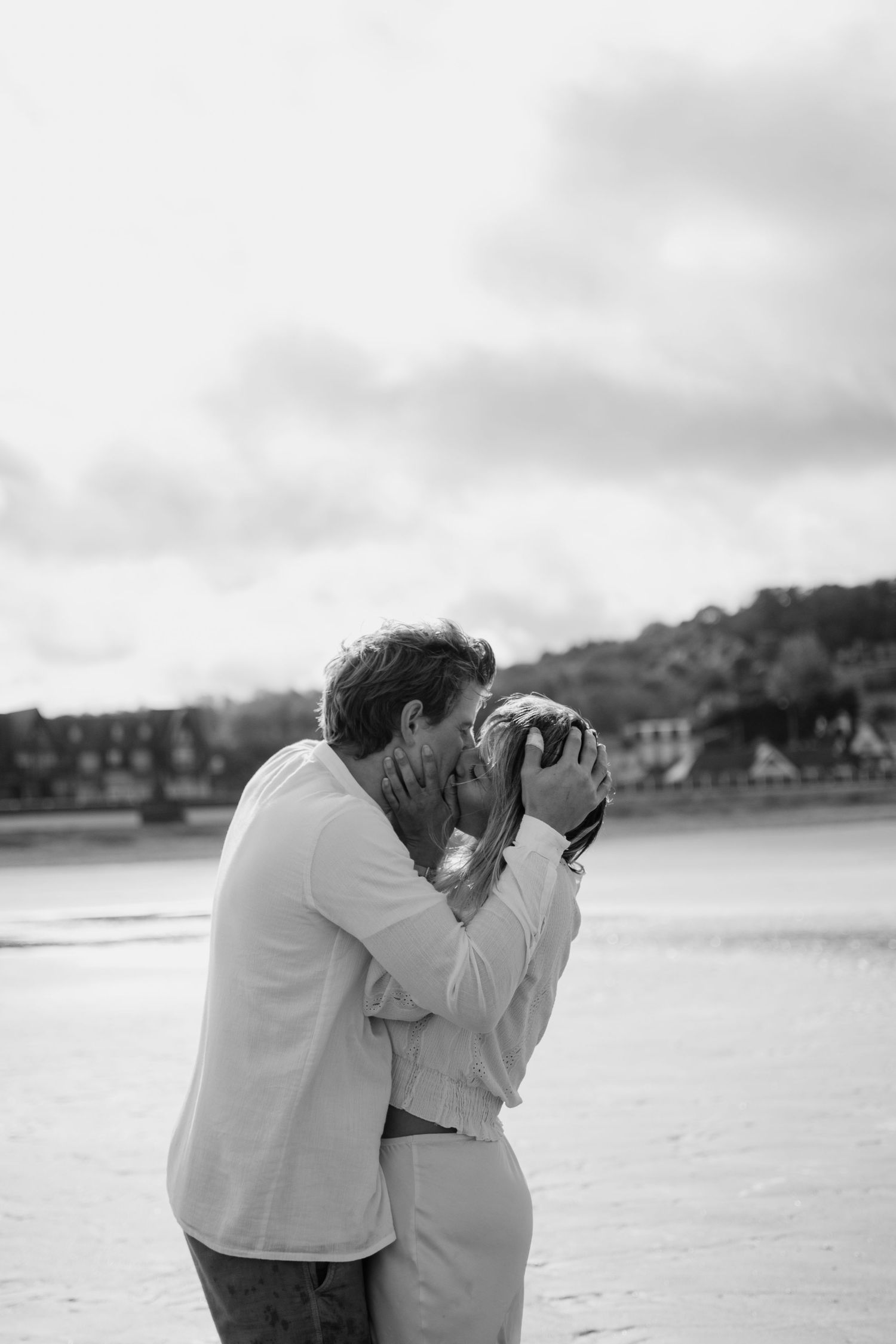 A romantic black and white photo of a couple sharing an intimate moment on a beach.