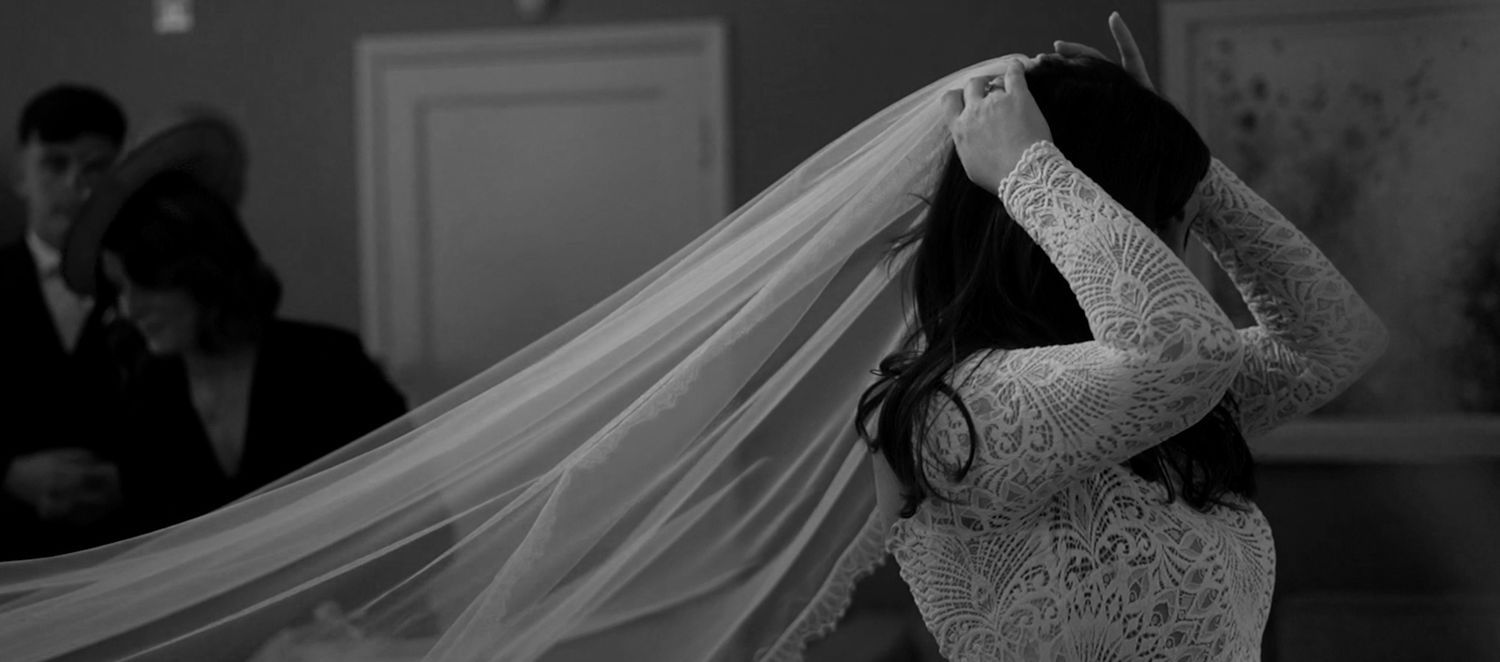 Bride in lace wedding dress adjusting her flowing veil in a black and white wedding photo.
