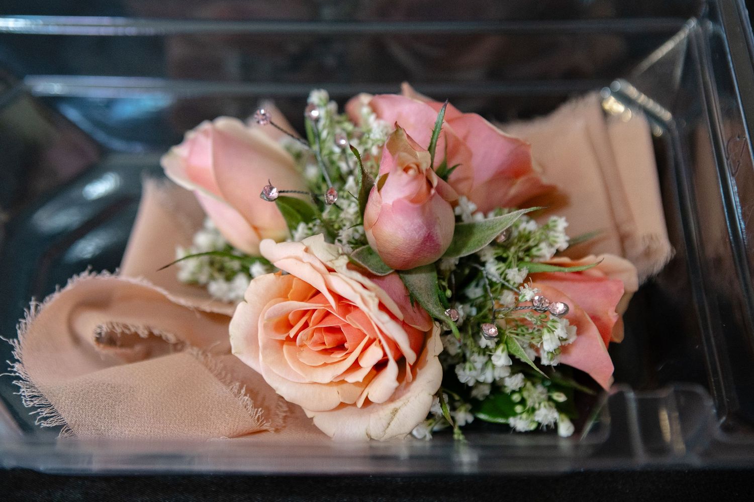 Delicate pink roses and baby's breath arranged with greenery on peach-colored fabric.