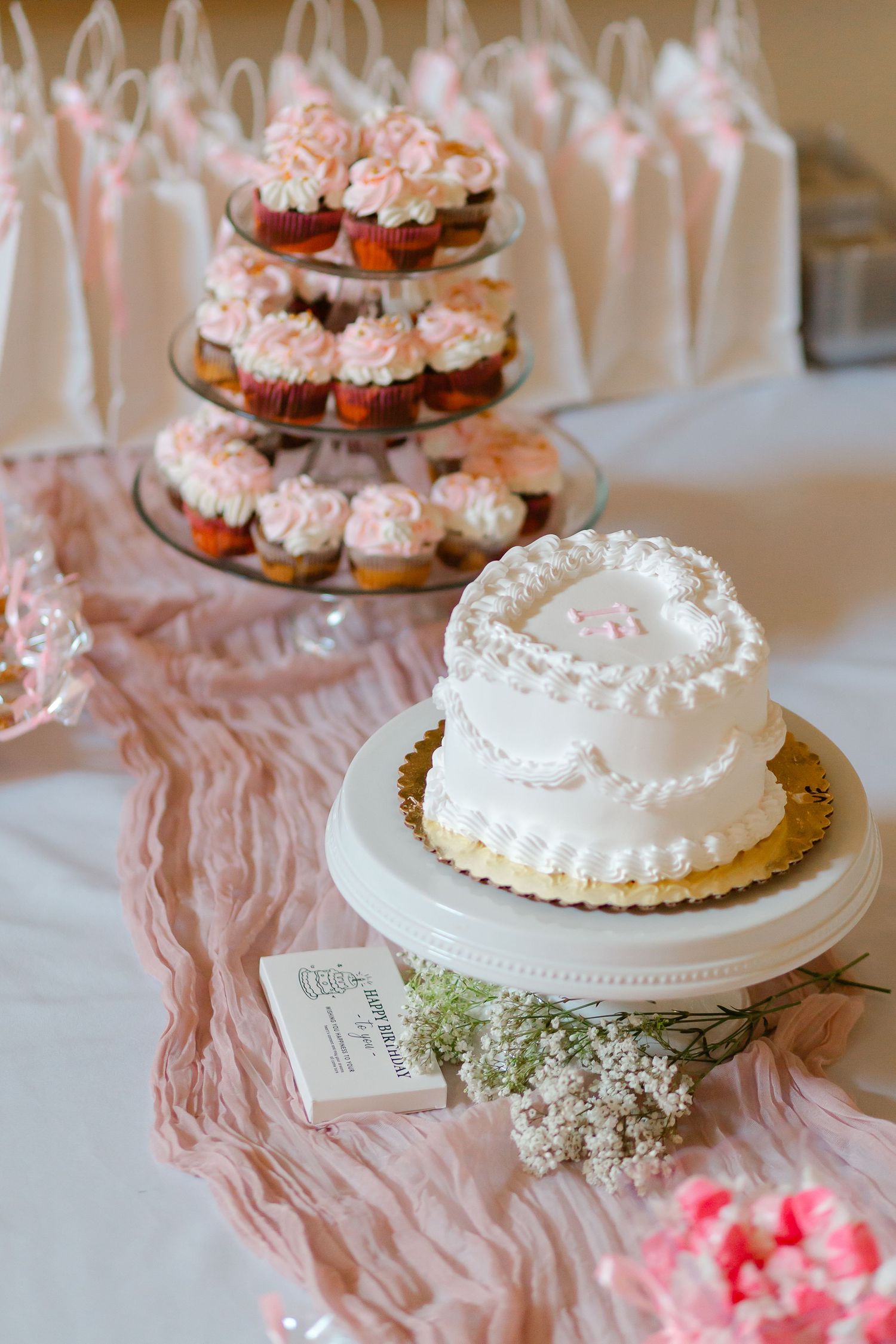 Tiered display of pink cupcakes and white wedding cake with lace detail.