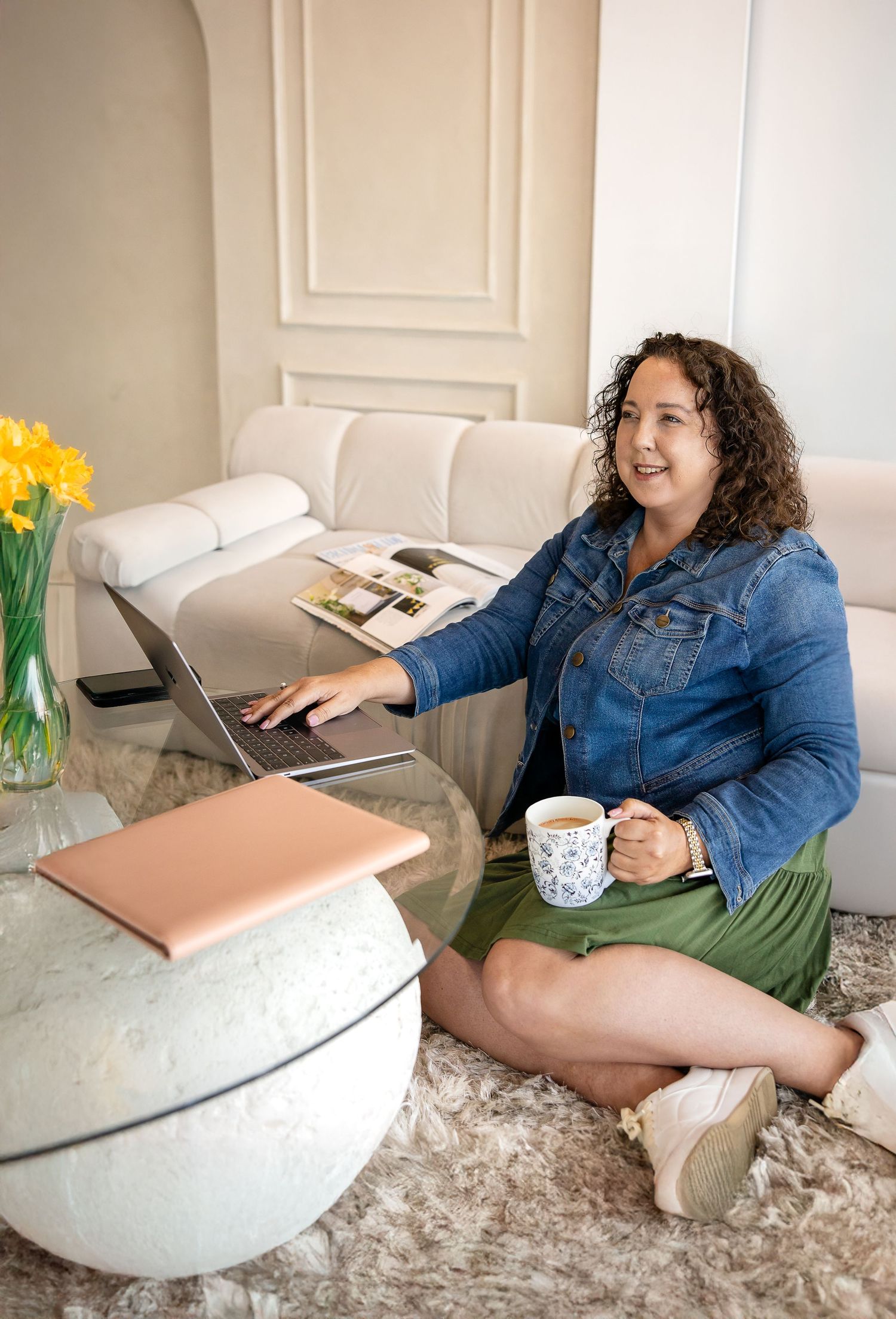 A remote worker sitting comfortably on a sofa with a laptop, coffee mug and spring daffodils nearby.
