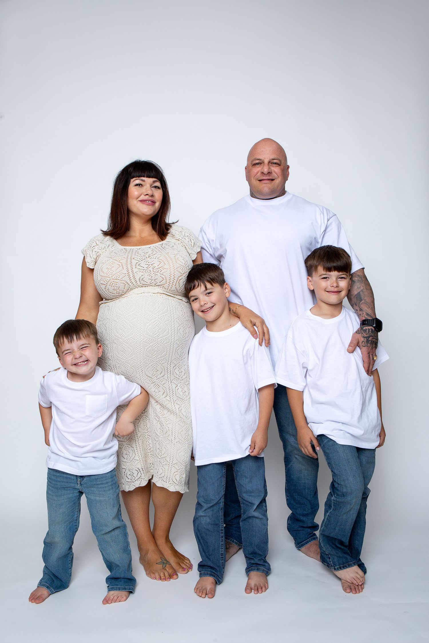 Studio family portrait with matching white shirts and blue jeans against light gray background.