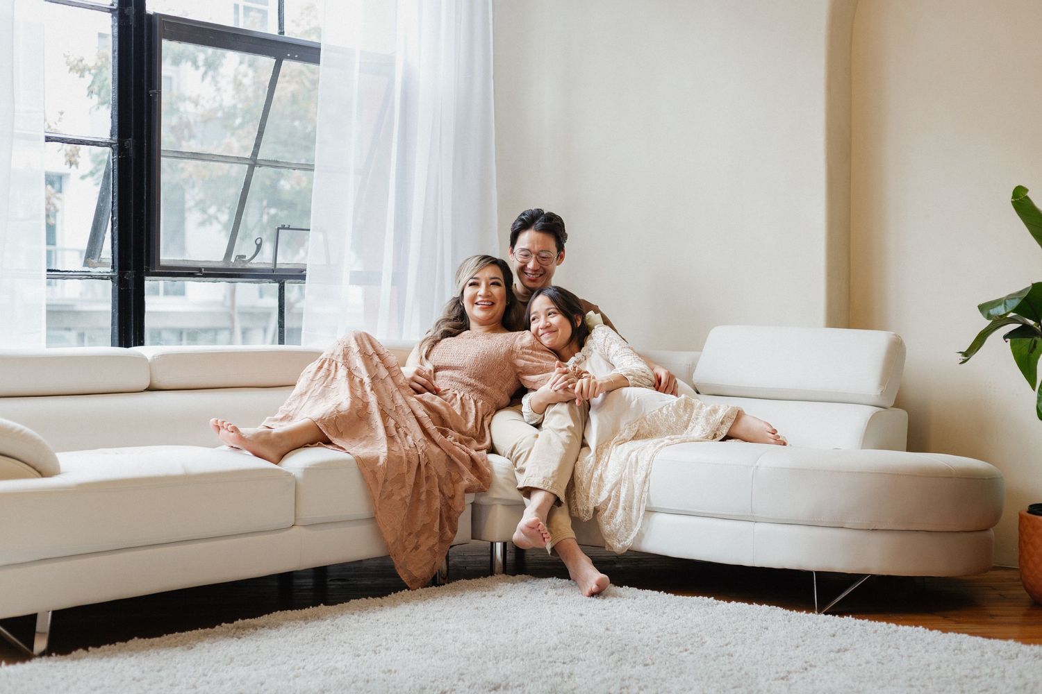 Happy family relaxing together on modern white couch in sunlit room.