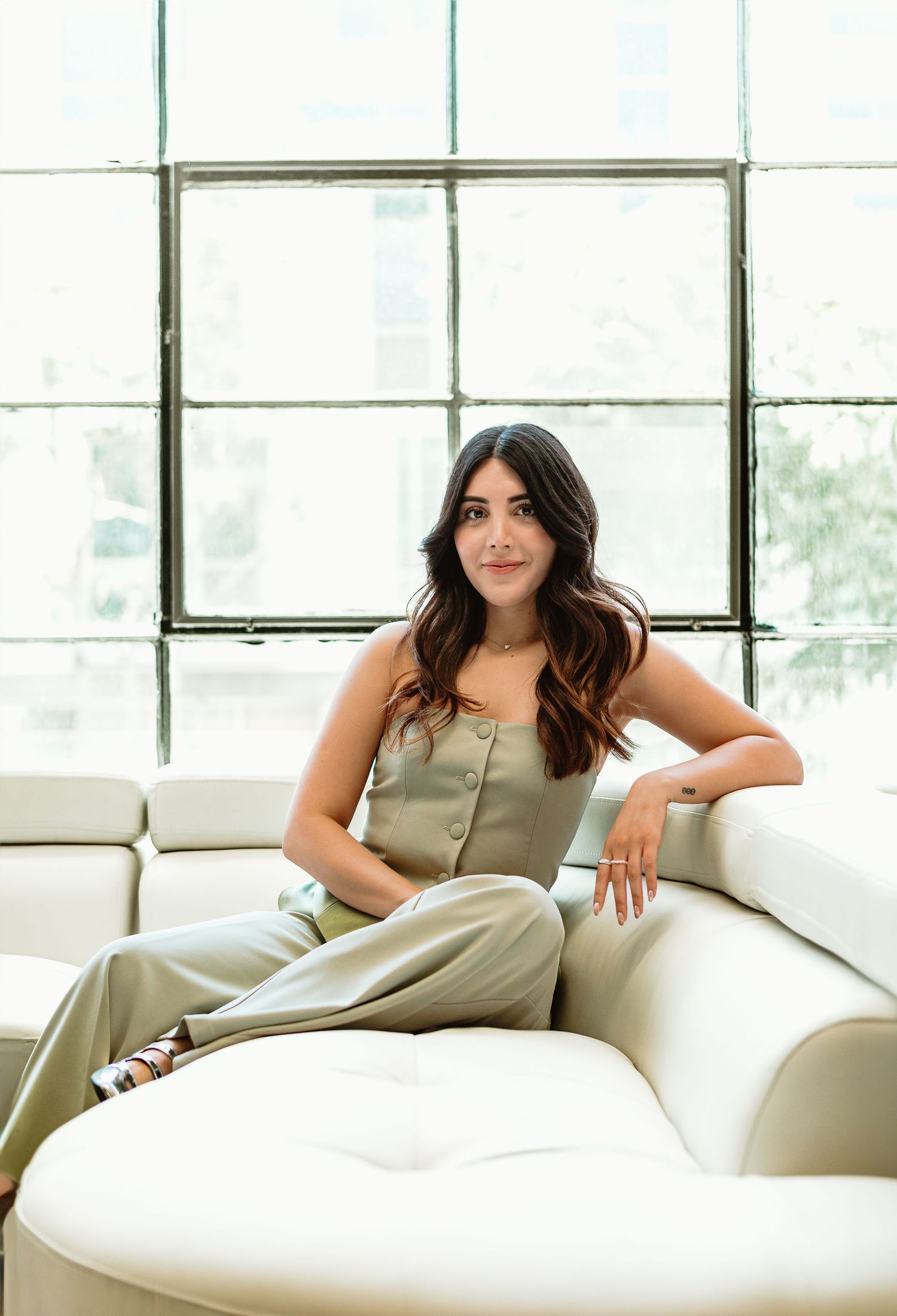 Casual portrait on white leather sofa with large windows and natural lighting.