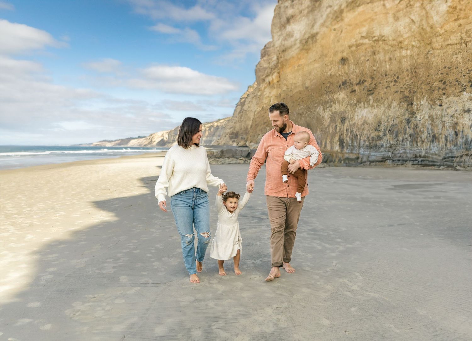 Family enjoys quality time together walking and playing on a scenic beach next to towering coastal cliffs.