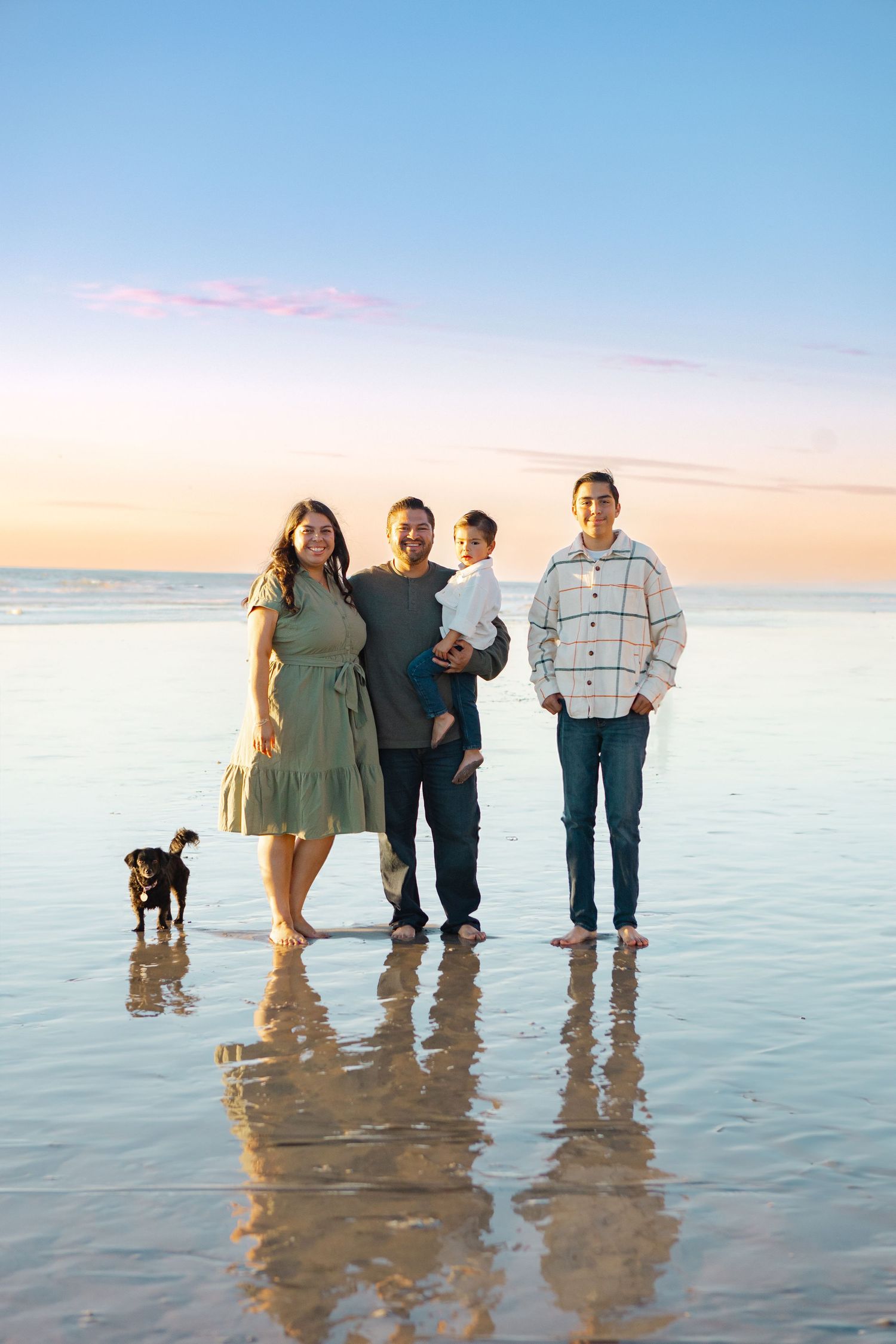 Family and dog standing together at beach during sunset.