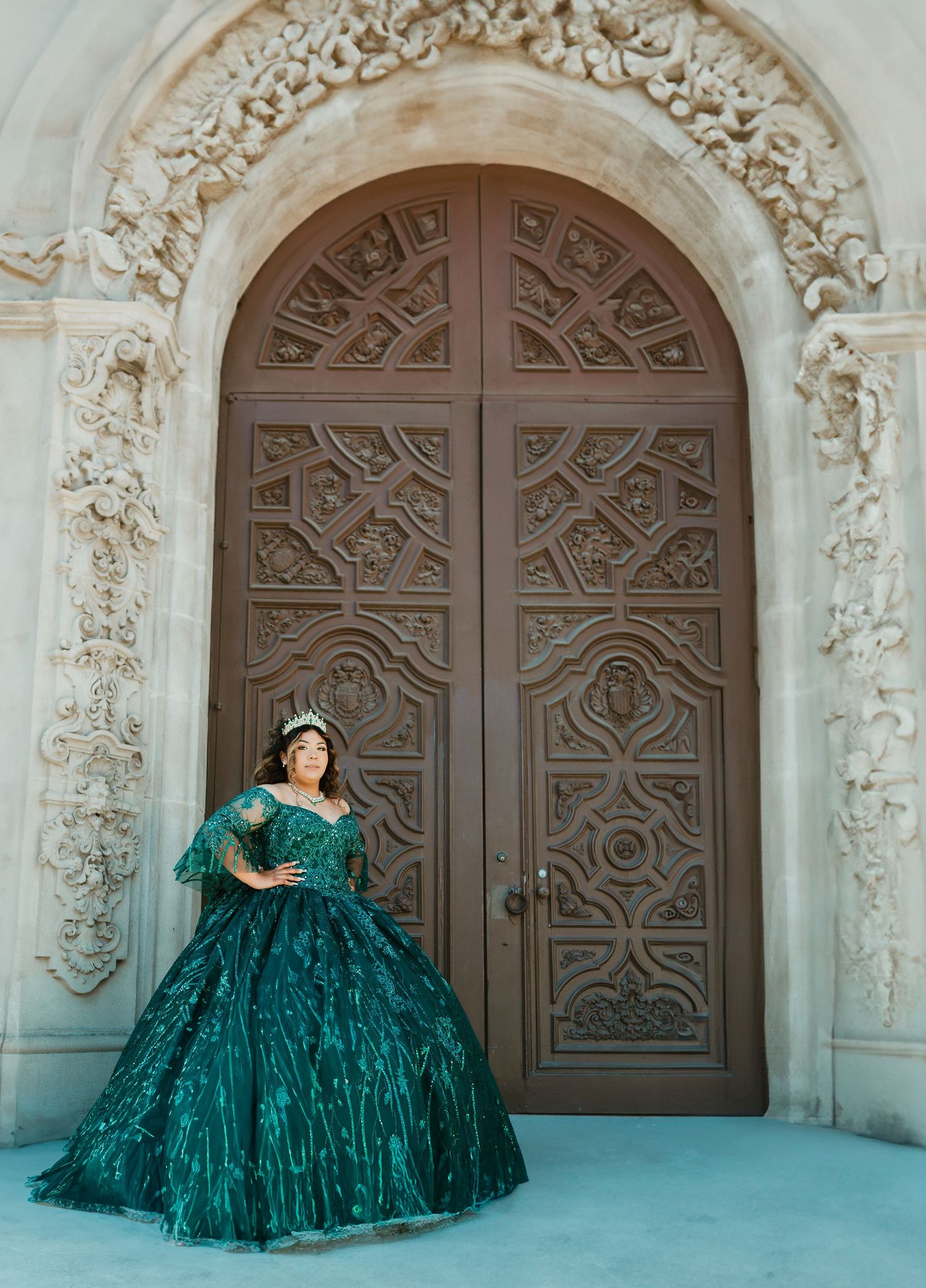 Emerald ball gown photographed against ornately carved stone doorway with religious motifs.