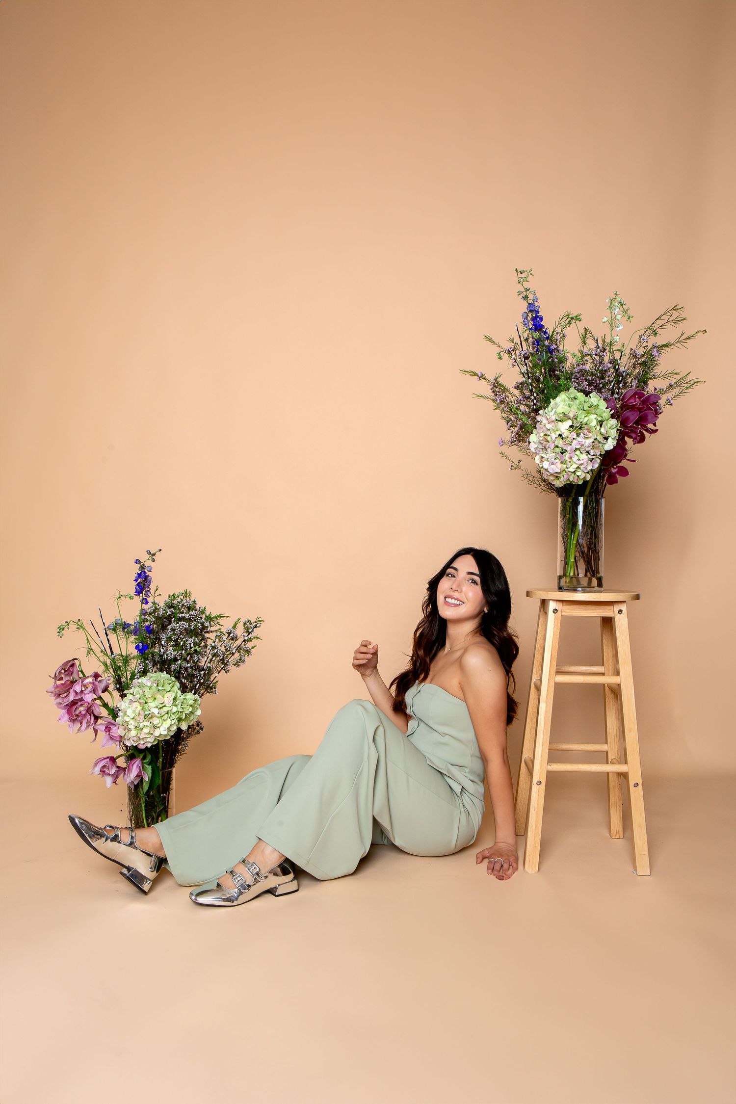 Lifestyle photo with floral arrangements and woman in mint green outfit against beige backdrop.