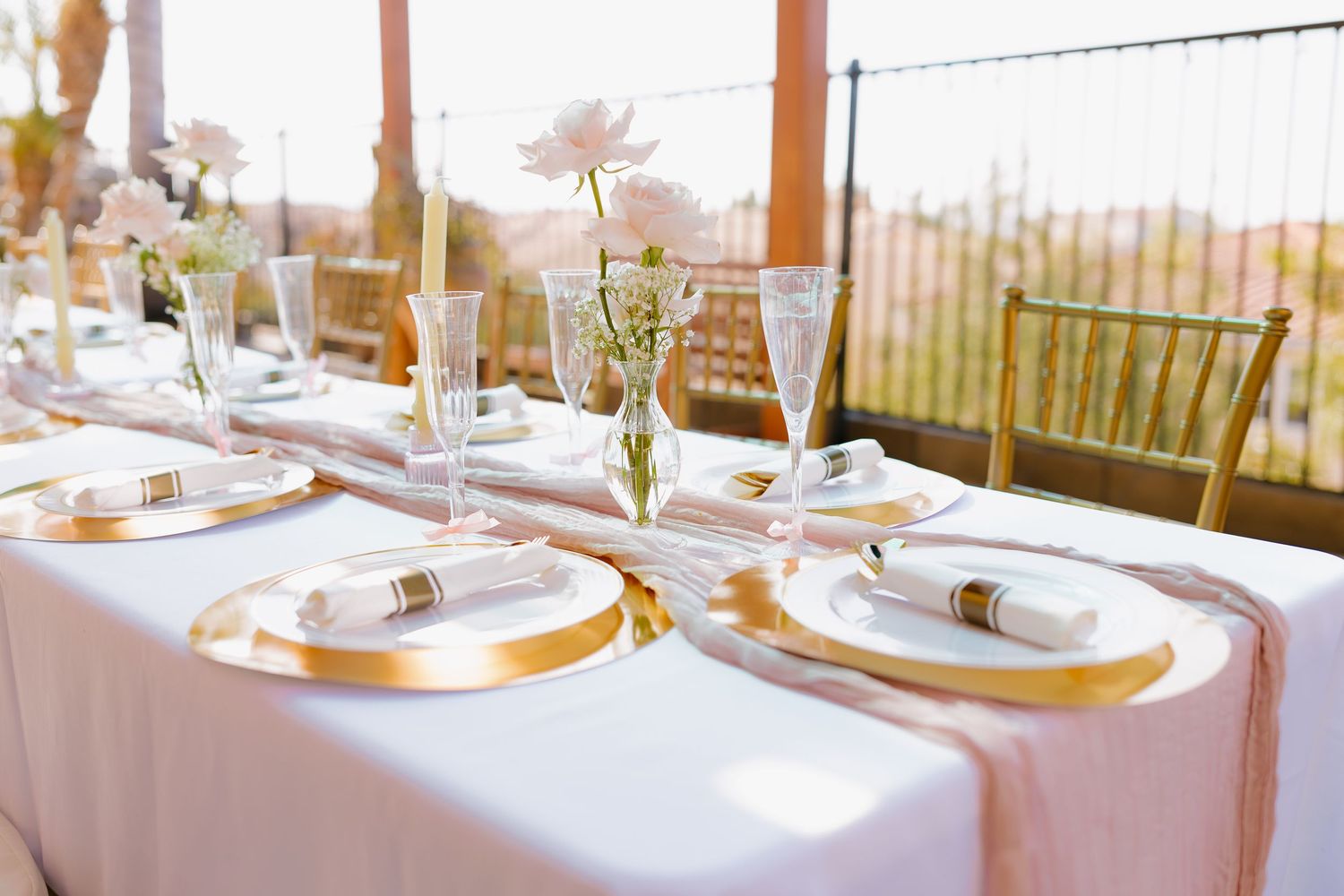 Elegant wedding table setting with gold chargers and white linens in golden sunlight.