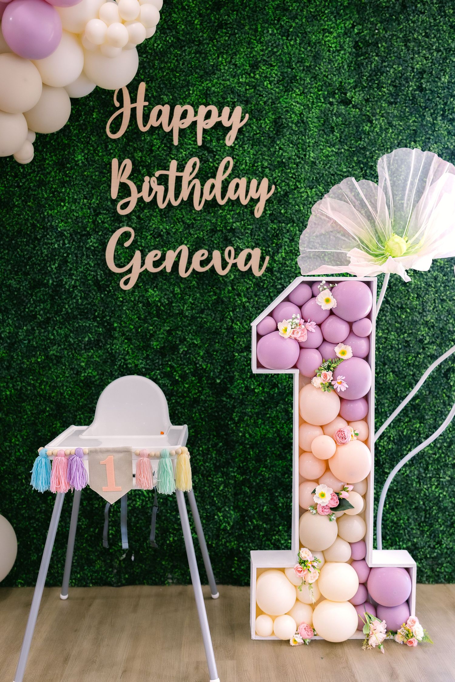 First birthday party decoration with balloon number one and green hedge wall backdrop.