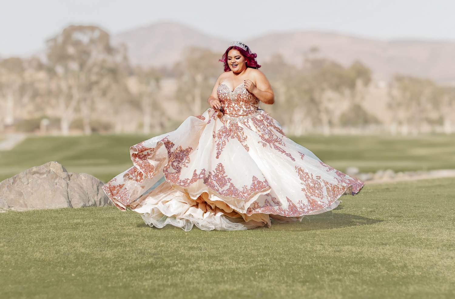 Flowing pink princess ball gown twirling on a green golf course with mountains in background.