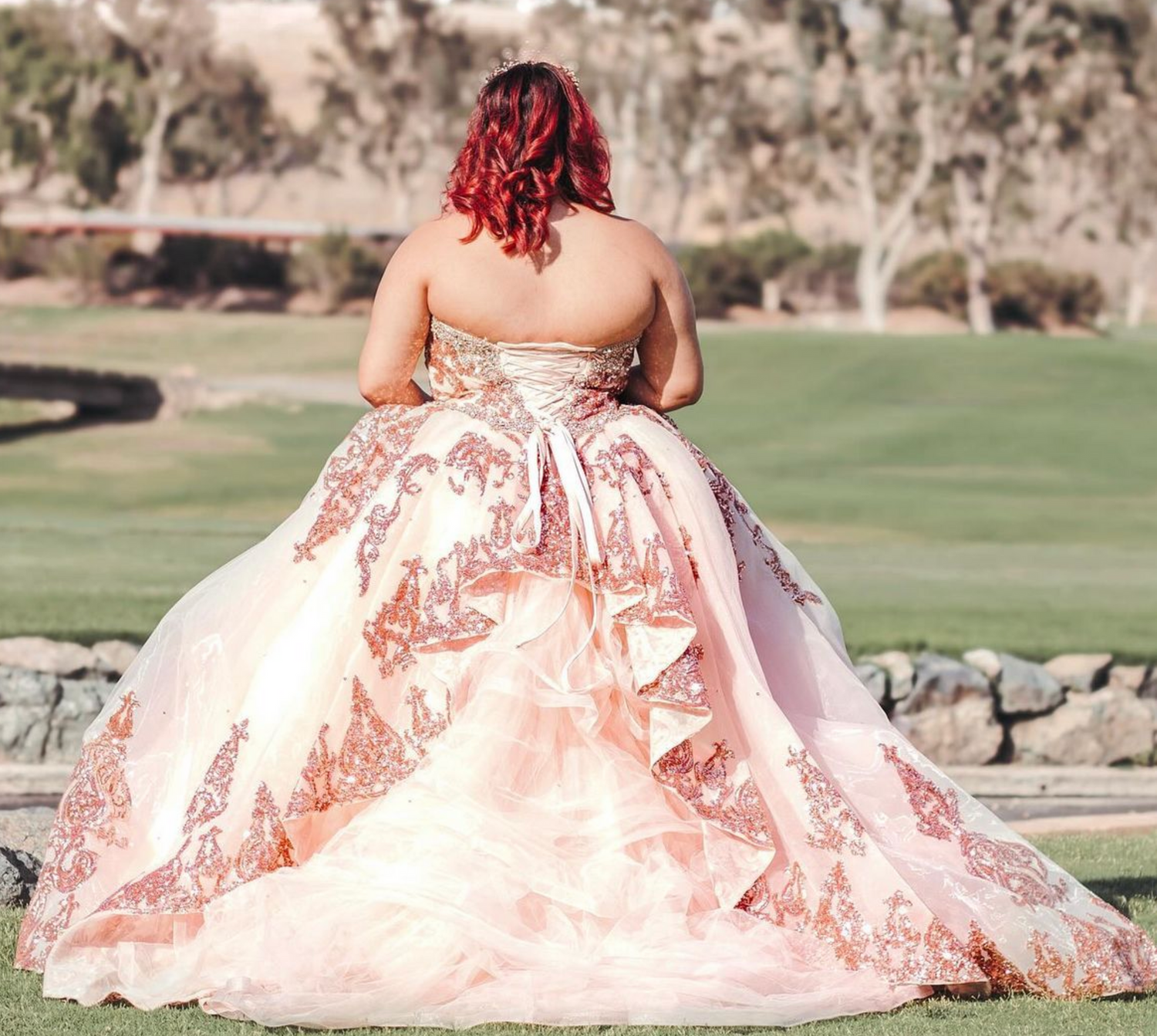 Elegant ball gown with rose gold appliques shown from behind on a scenic golf course.