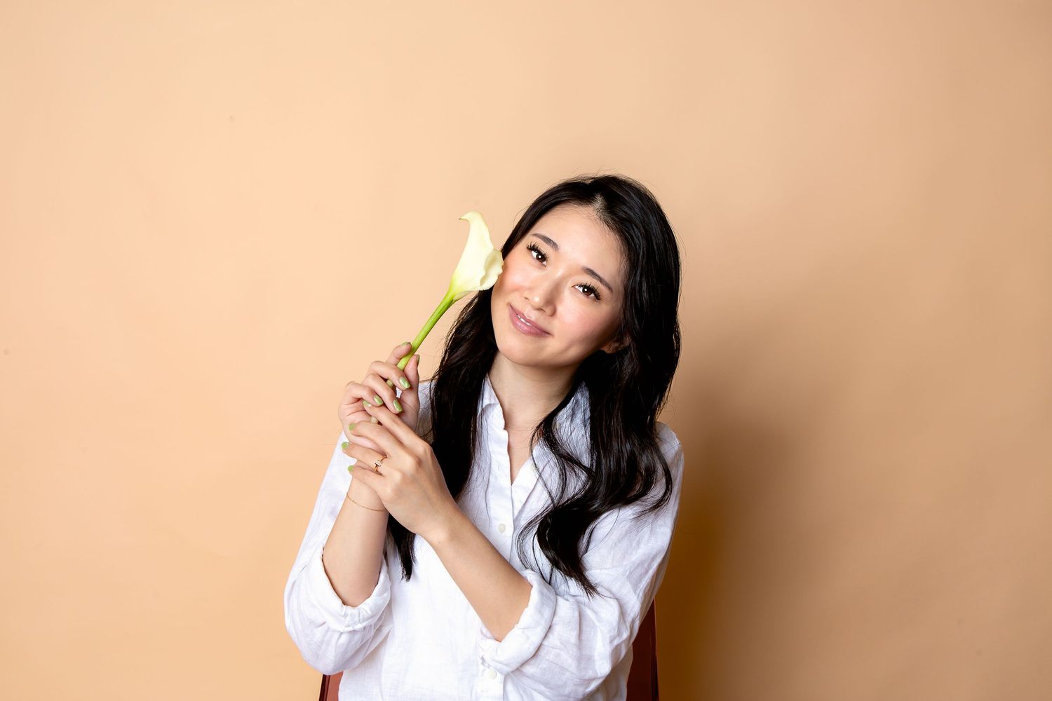 Person in white button-down shirt holding a bright yellow banana against peach-colored background.