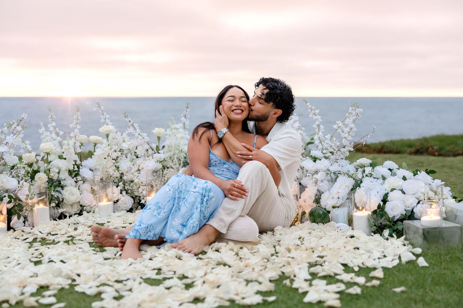 A couple embraces among elegant white floral arrangements at an outdoor garden venue during a romantic photoshoot.