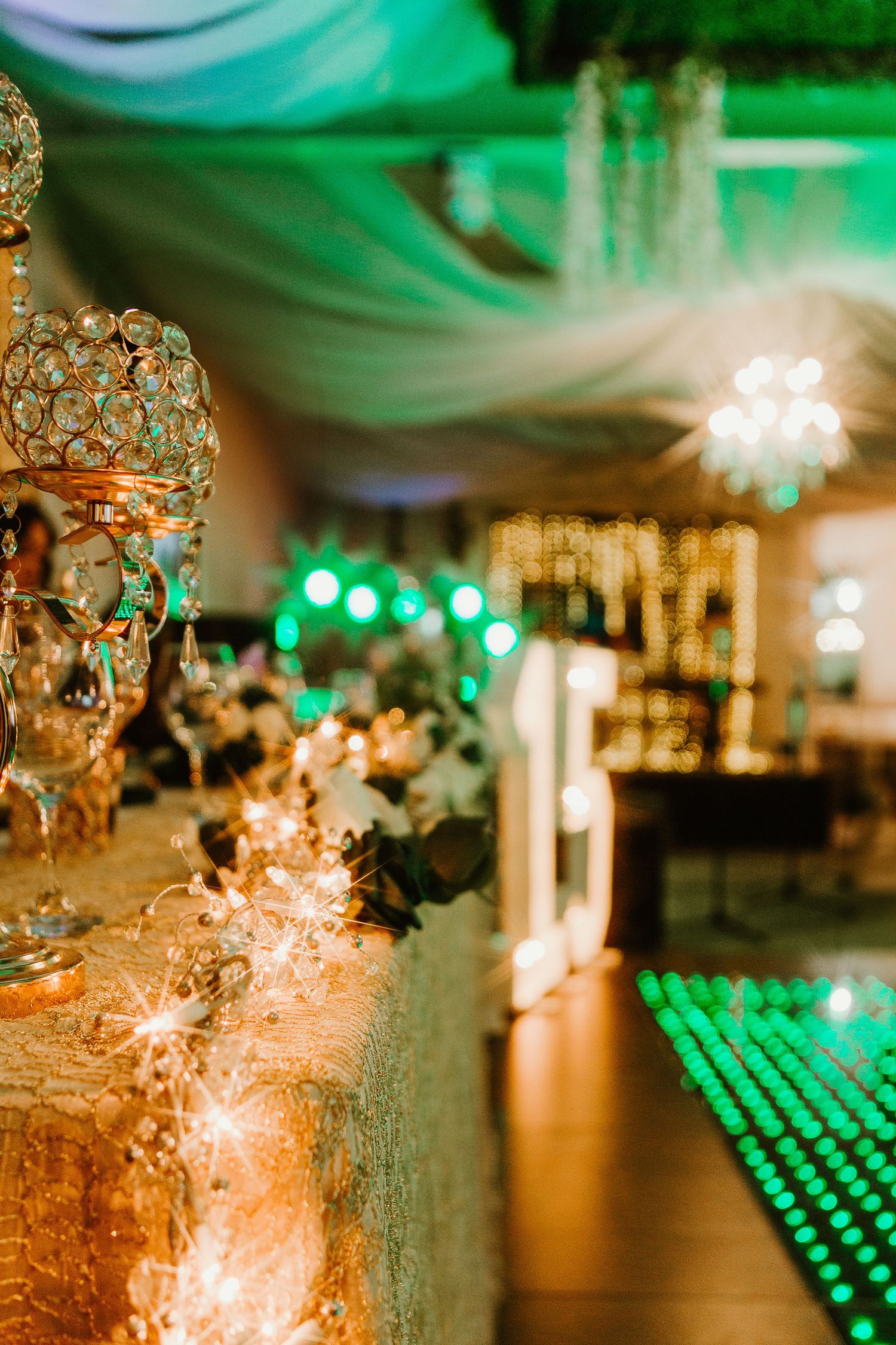 Elegant reception venue with crystal chandelier and green ambient lighting creating romantic atmosphere.