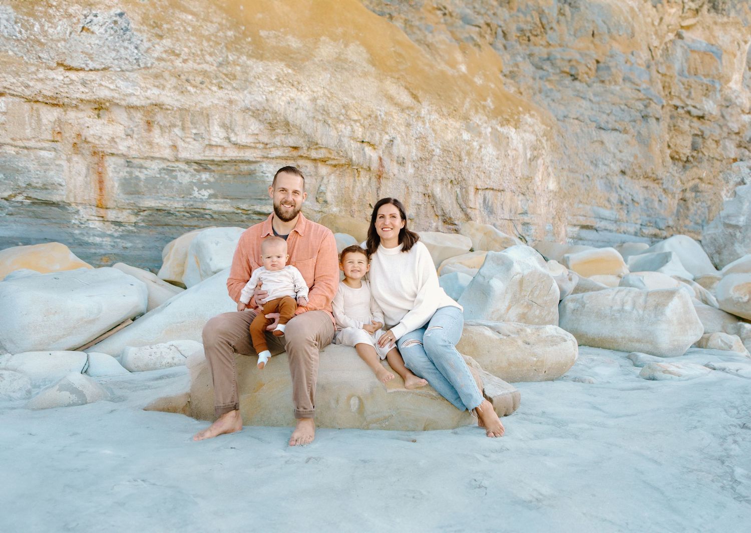 Family sitting together on blue rocks at a scenic beach location.