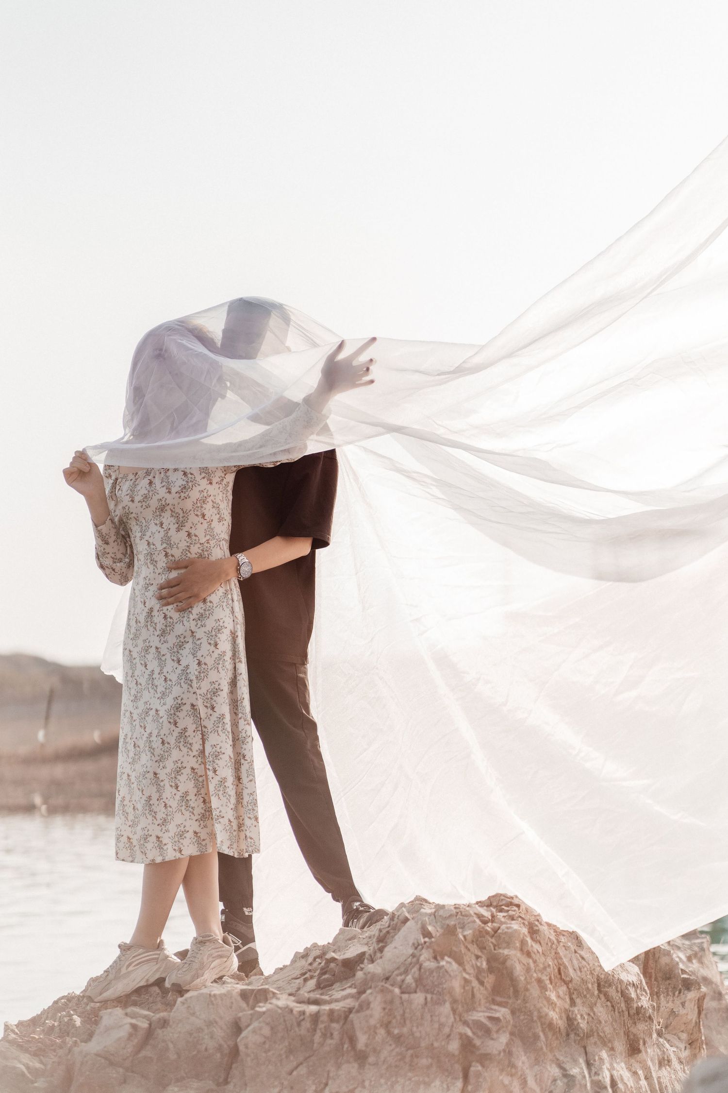 A man and woman holding a wedding veil being swept away by the wind