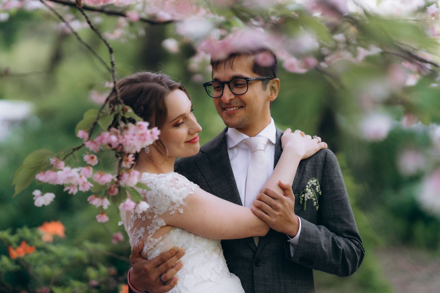 A couple shares a romantic dance moment under blooming cherry blossom trees in a garden setting.
