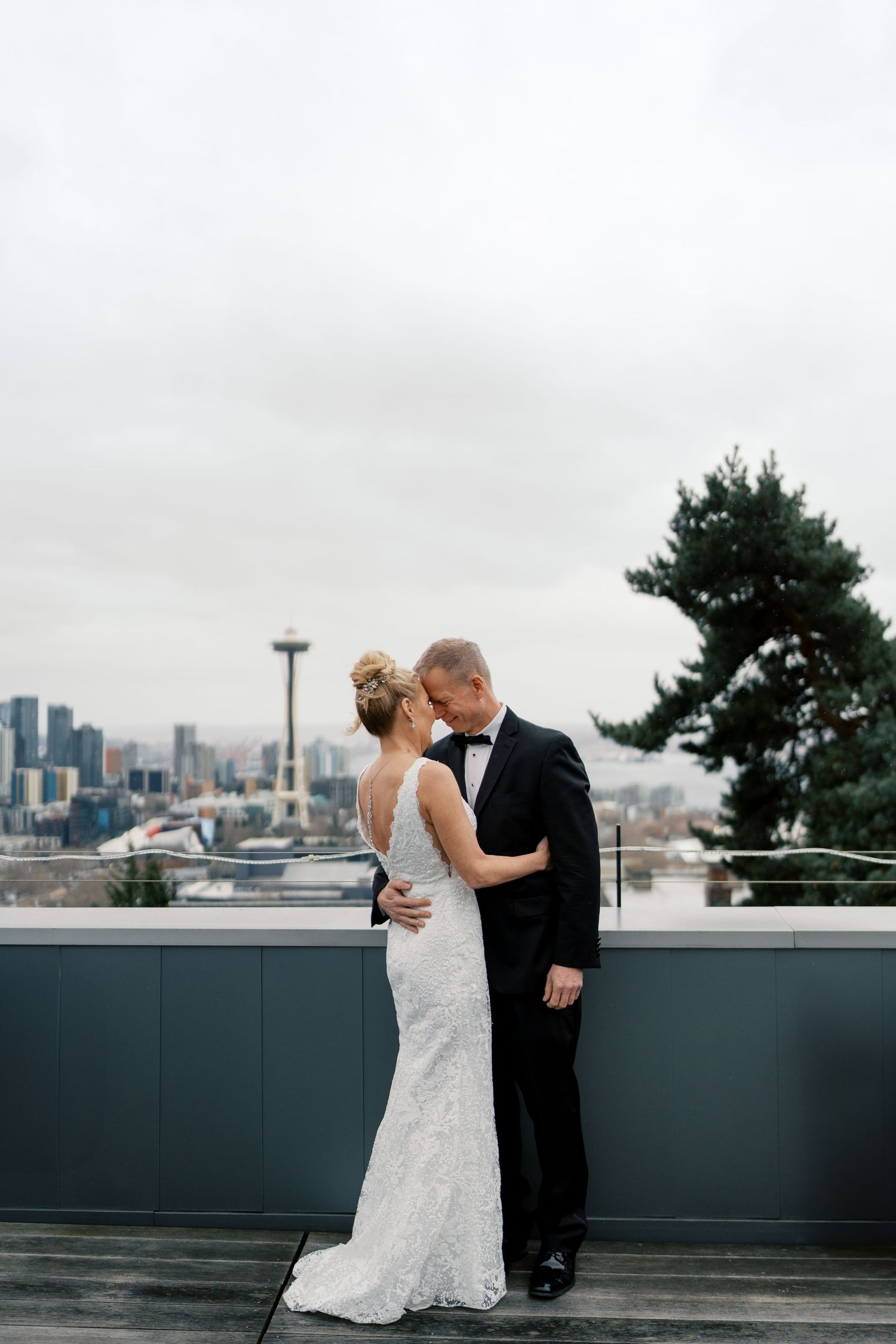Newlywed couple sharing a romantic moment on a rooftop with Seattle skyline and Space Needle in background.