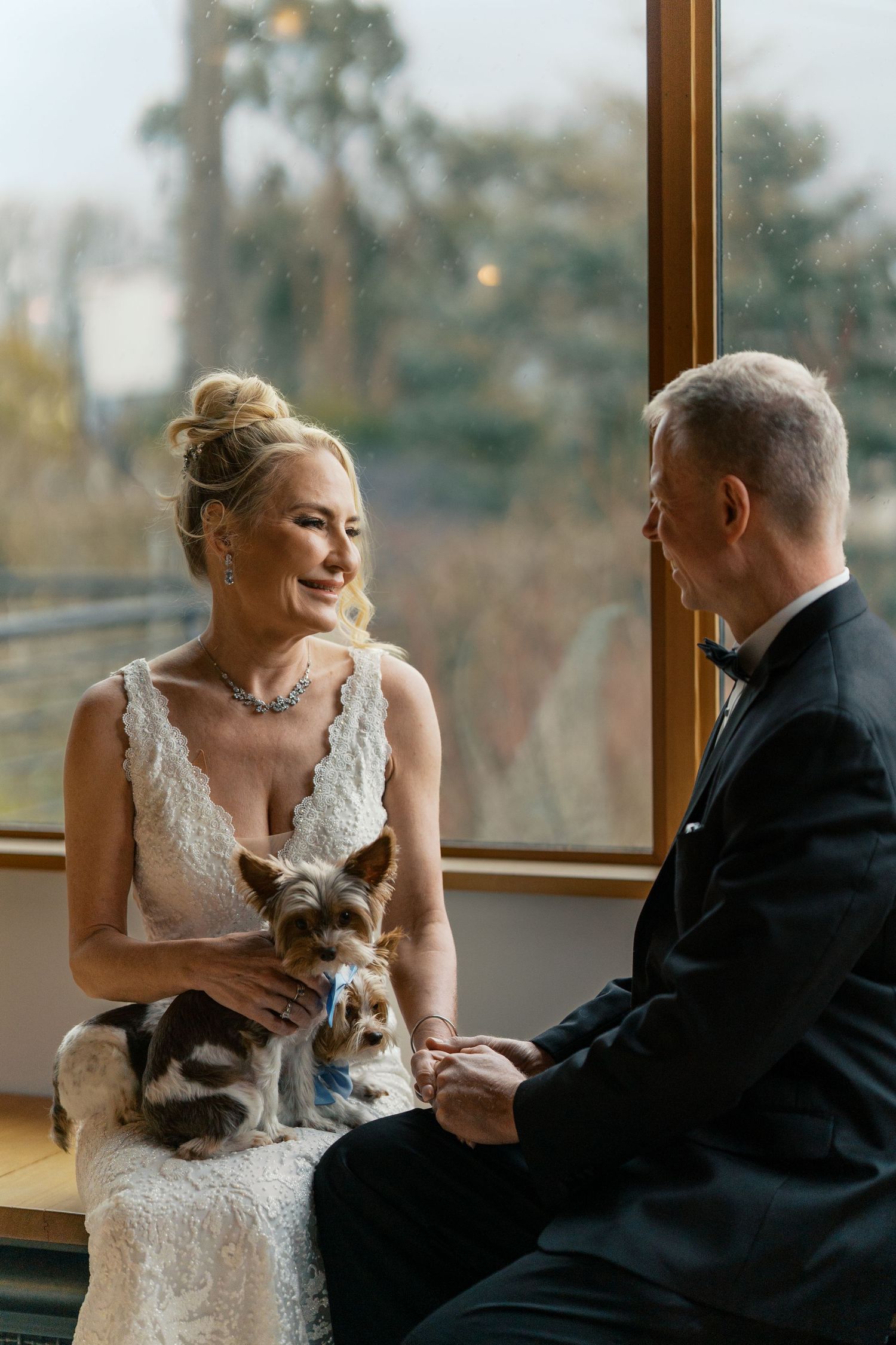 A couple shares an intimate moment together on a couch by large windows while their cat joins them in sweet companionship.