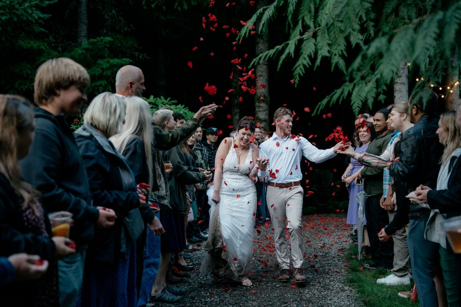 People gather and dance together in a celebratory manner in an outdoor garden setting at dusk.