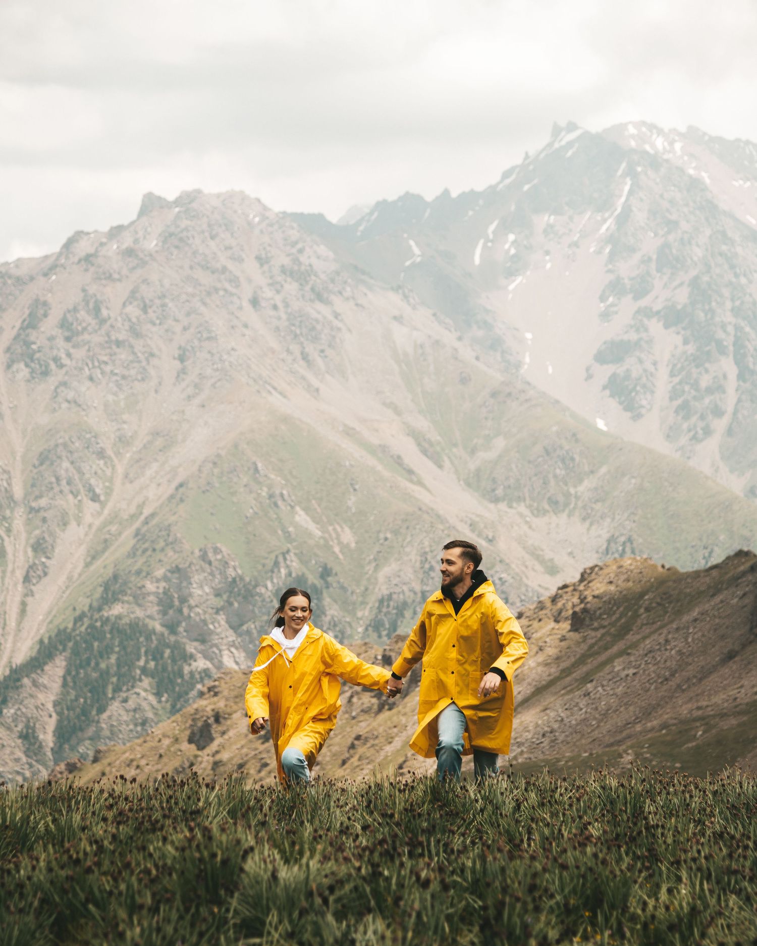 A man and woman wearing matching yellow rain jackets running in the fall mountains