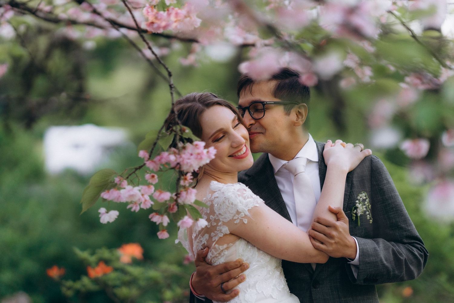 Couple shares tender moments among blooming pink cherry blossoms in a romantic spring wedding photoshoot.
