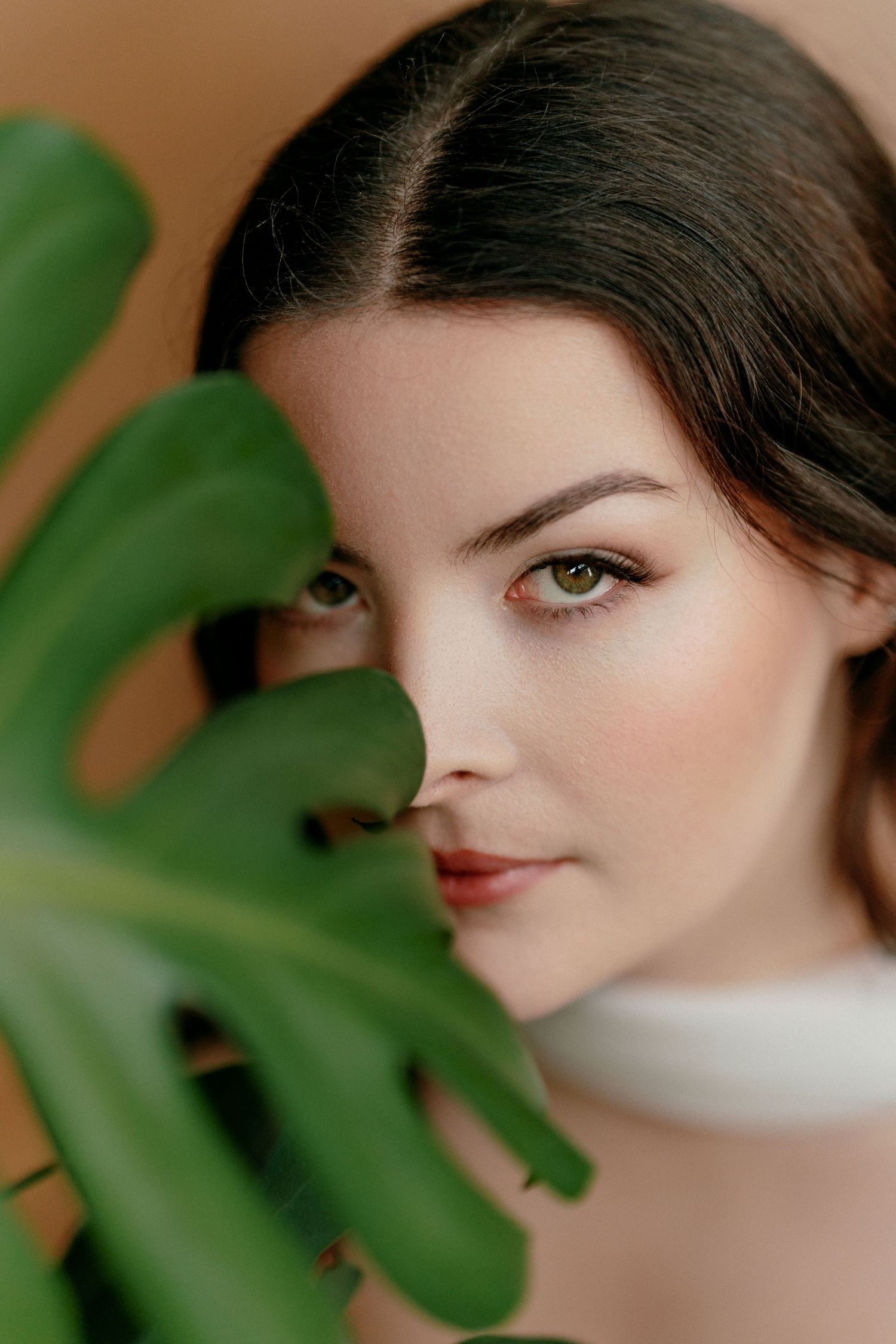 A portrait composition with green monstera leaves in the foreground adding a natural element to the soft beauty shot.