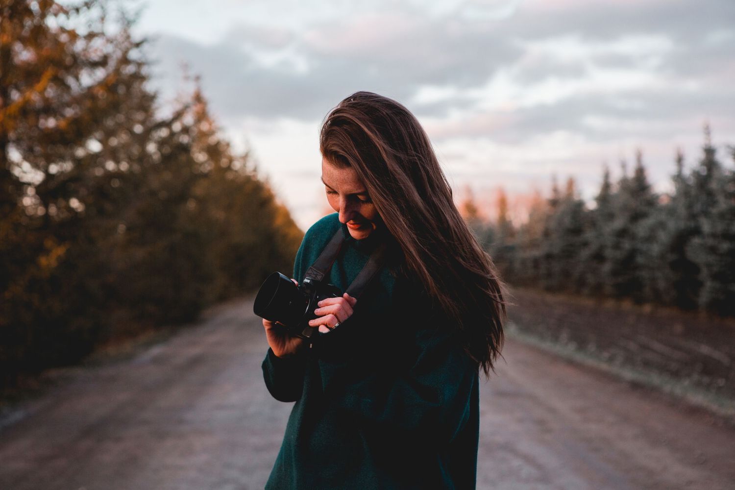 Silhouetted person walking along a winding path during sunset with trees and cloudy sky in background.